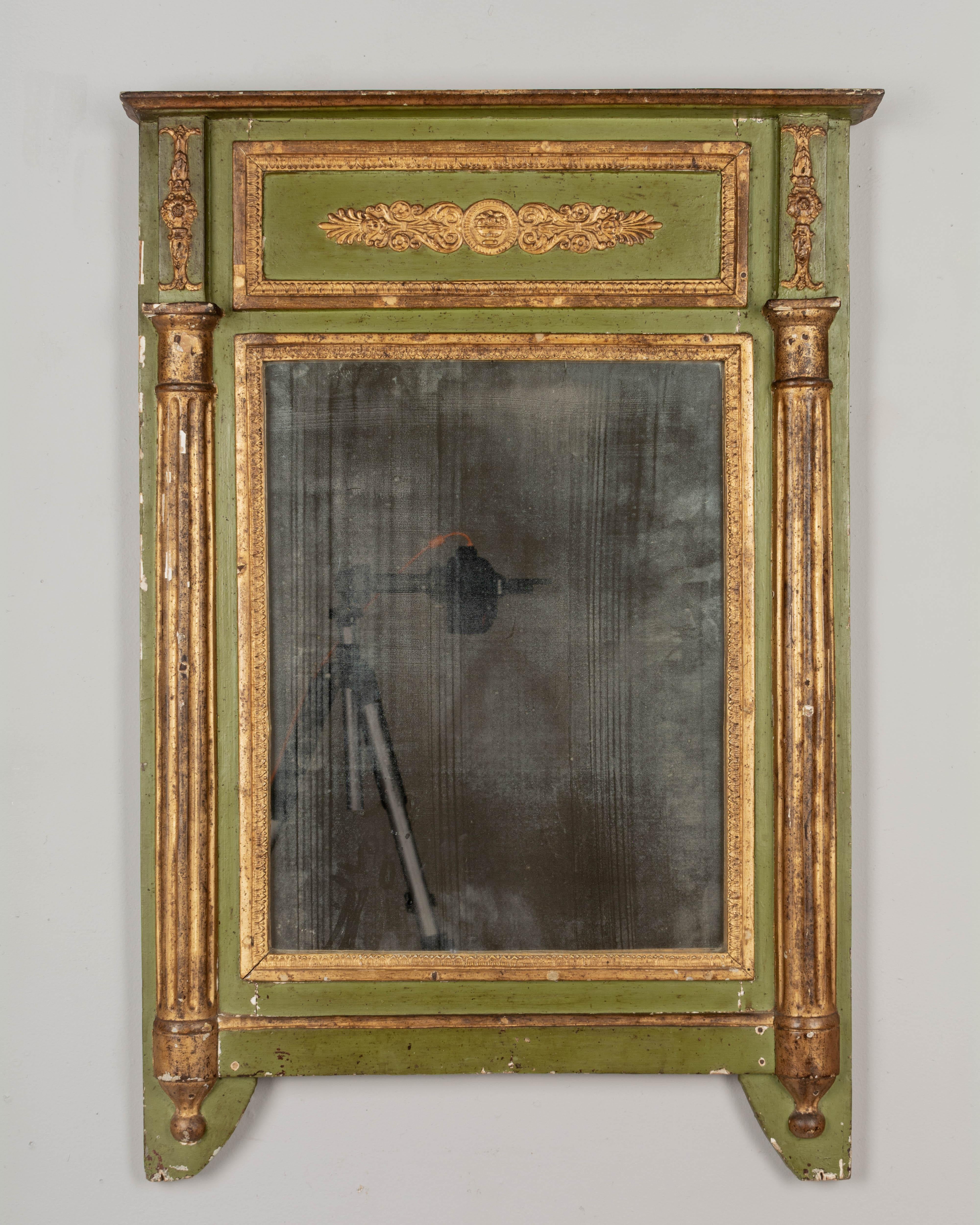 An early 19th century French directoire period parcel gilt mirror. Architectural green painted frame with three dimensional fluted columns and a gilt frieze decorated in low relief. Original mirror with fogged patina. Original finish with losses