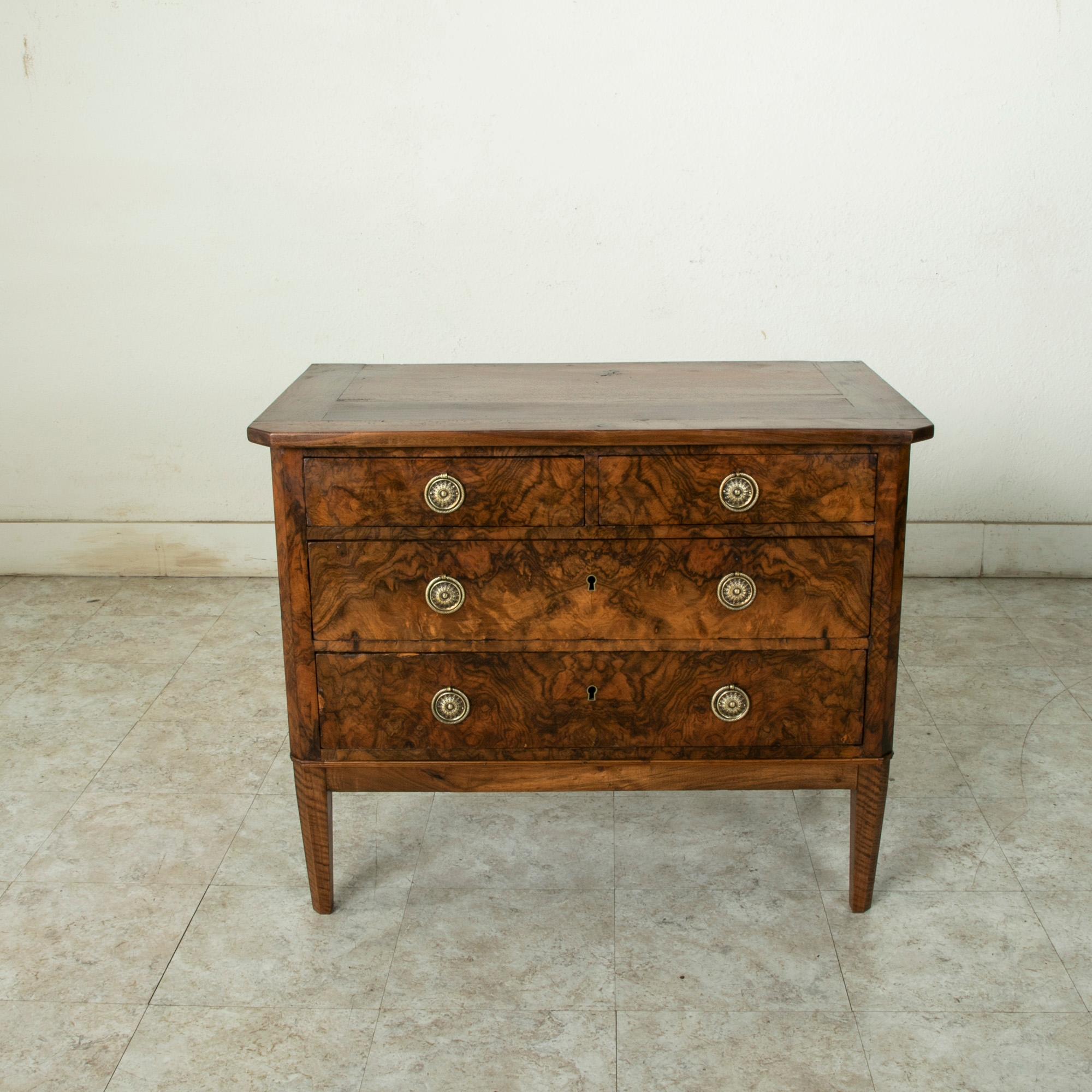 This mid-19th century French Directoire style commode or chest of drawers features a bookmatched burl walnut facade. Its solid walnut top rests above three drawers of dovetail construction. The drawers are fitted with brass drop ring handles, and