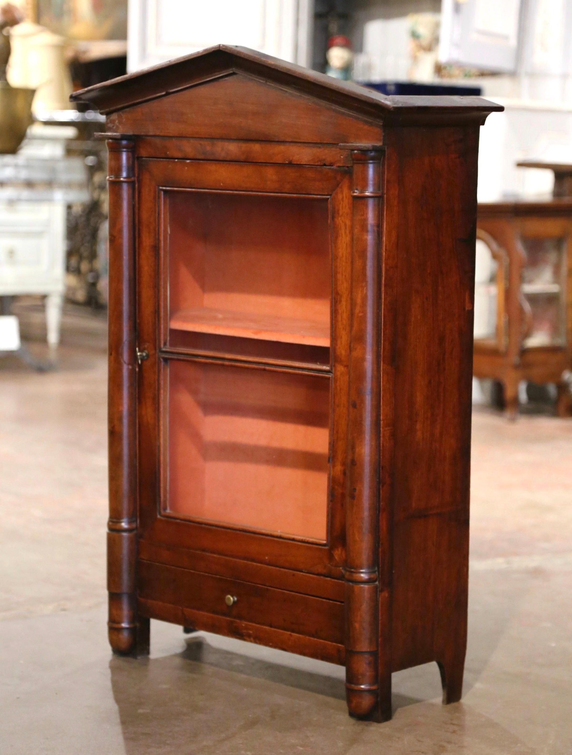 This elegant antique vitrine was crafted in southern France, circa 1830. The wall cabinet with roof shape bonnet top, is decorated with baluster columns on the sides. The curio cabinet features a single door with the original wavy glass panel and