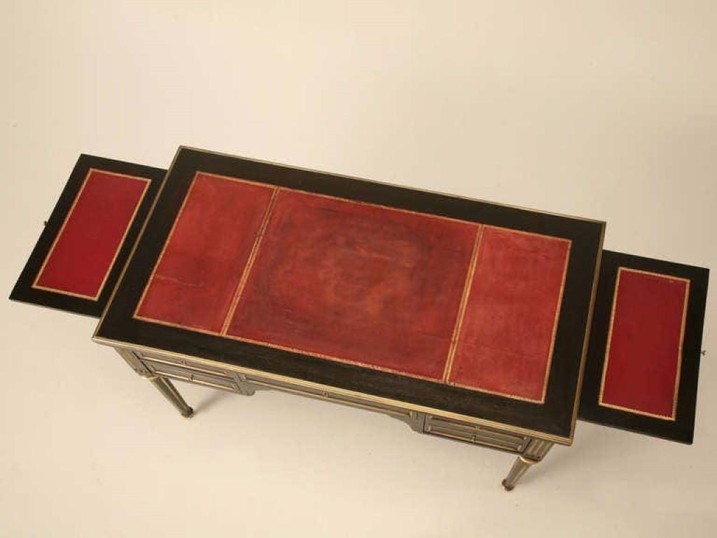 Circa 1880 antique French Napoleon III writing desk with its original leather top surface and brass details on turned fluted legs. Beautifully restored in a proper ebonized finish that still lets the color and texture of the mahogany show through