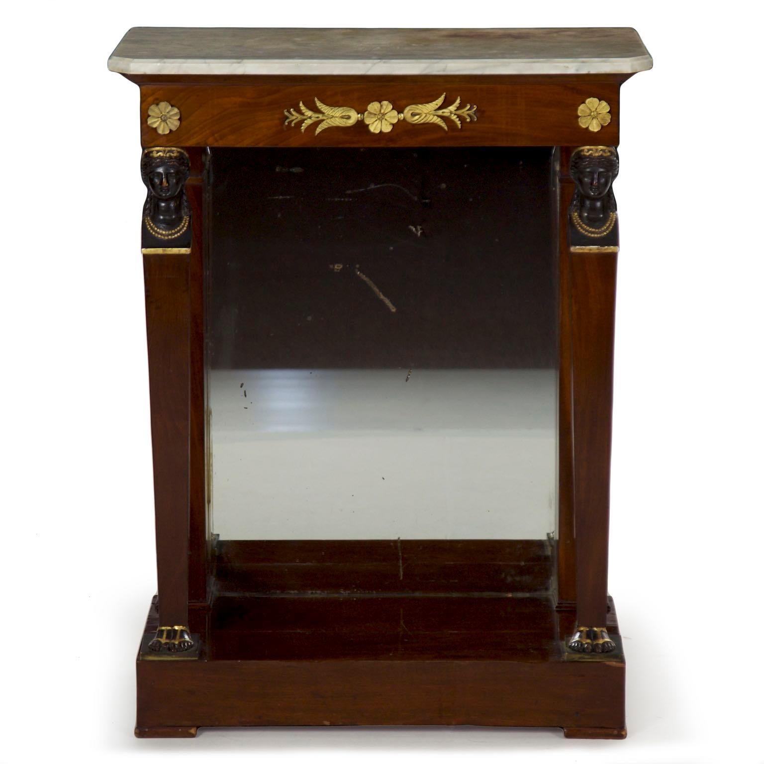 A striking pier table from the mid-late 19th century, the console is characterized by a pair of tapered columns with ebonized carved wood classical female figural masks raising a shallow apron with two gilt bronze rosettes flanking a broad anthemion
