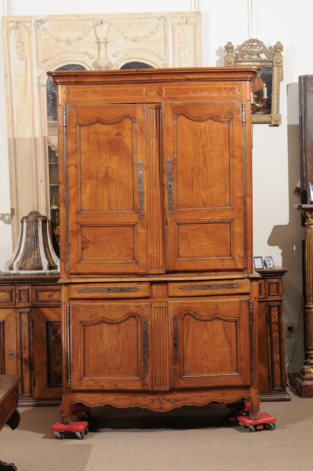 A 19th century French Transitional Louis XV and Louis XVI buffet deux corps in elm with carved fluting, inlay detail, 4 paneled doors with interior shelving and carved shaped apron ending on cabriole legs.