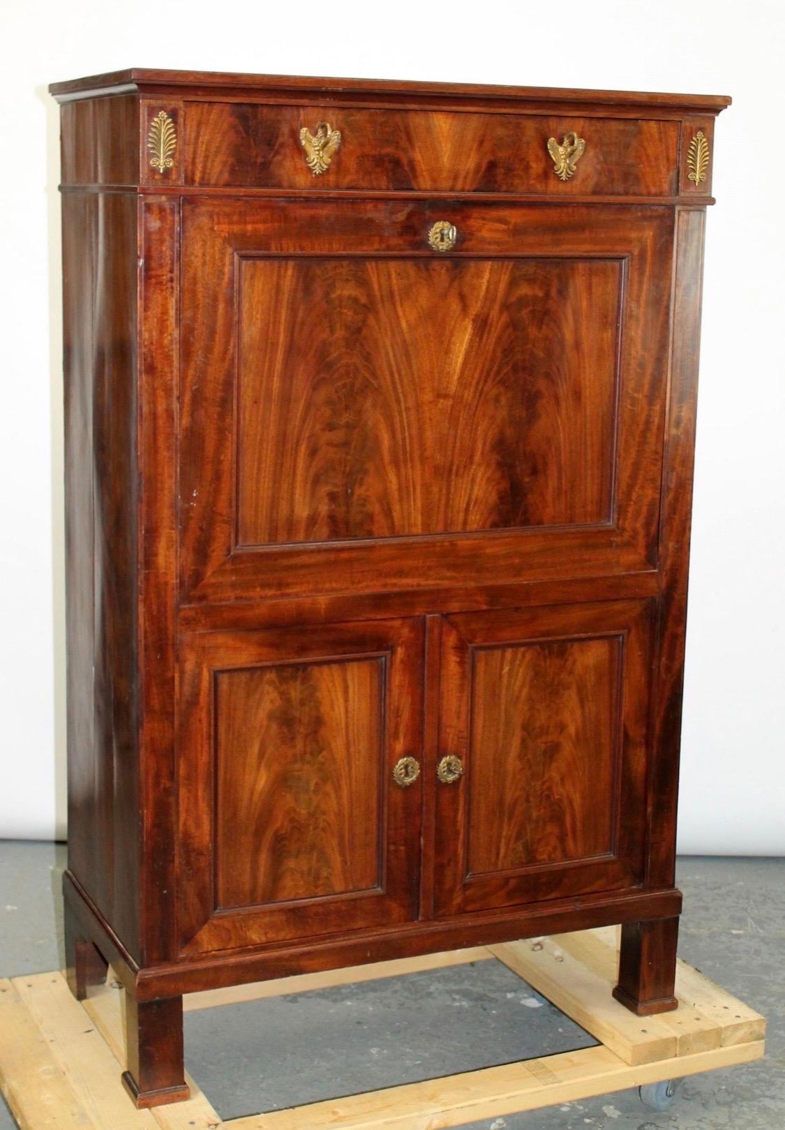 This French Empire Abattant Secretary Desk from the late 19th century is a striking piece of furniture, crafted from flame mahogany. The abattant (drop-front) design allows for a concealed writing surface when closed while opening to reveal a tooled