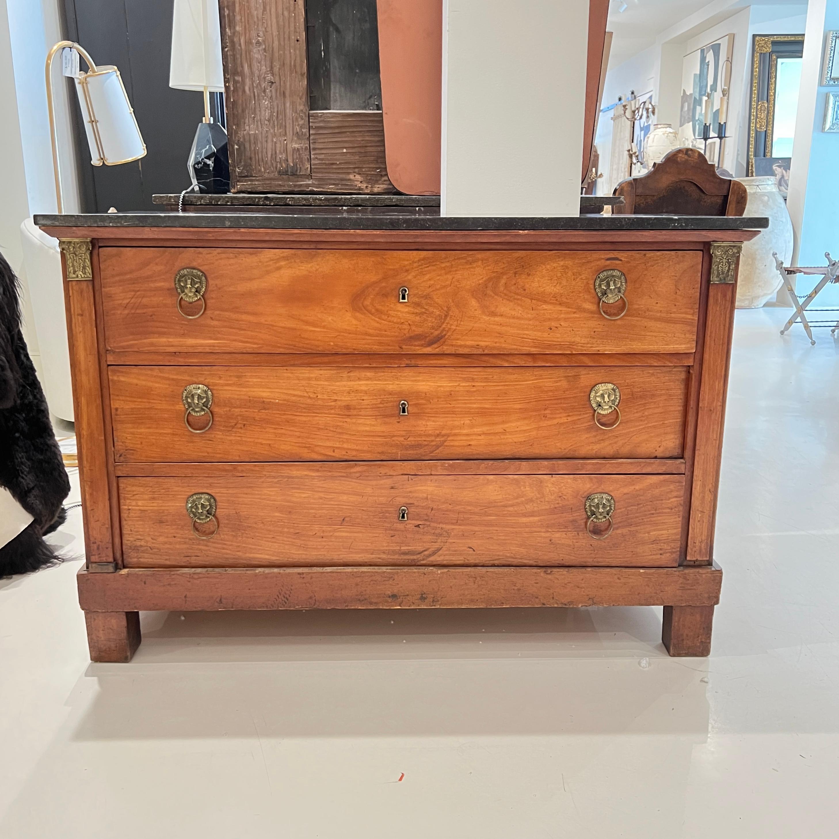 This French Empire chest features a rich wood grain, stately grey marble top, and striking lion-head pulls—embodying the grandeur and symmetry of early 19th-century neoclassical design.