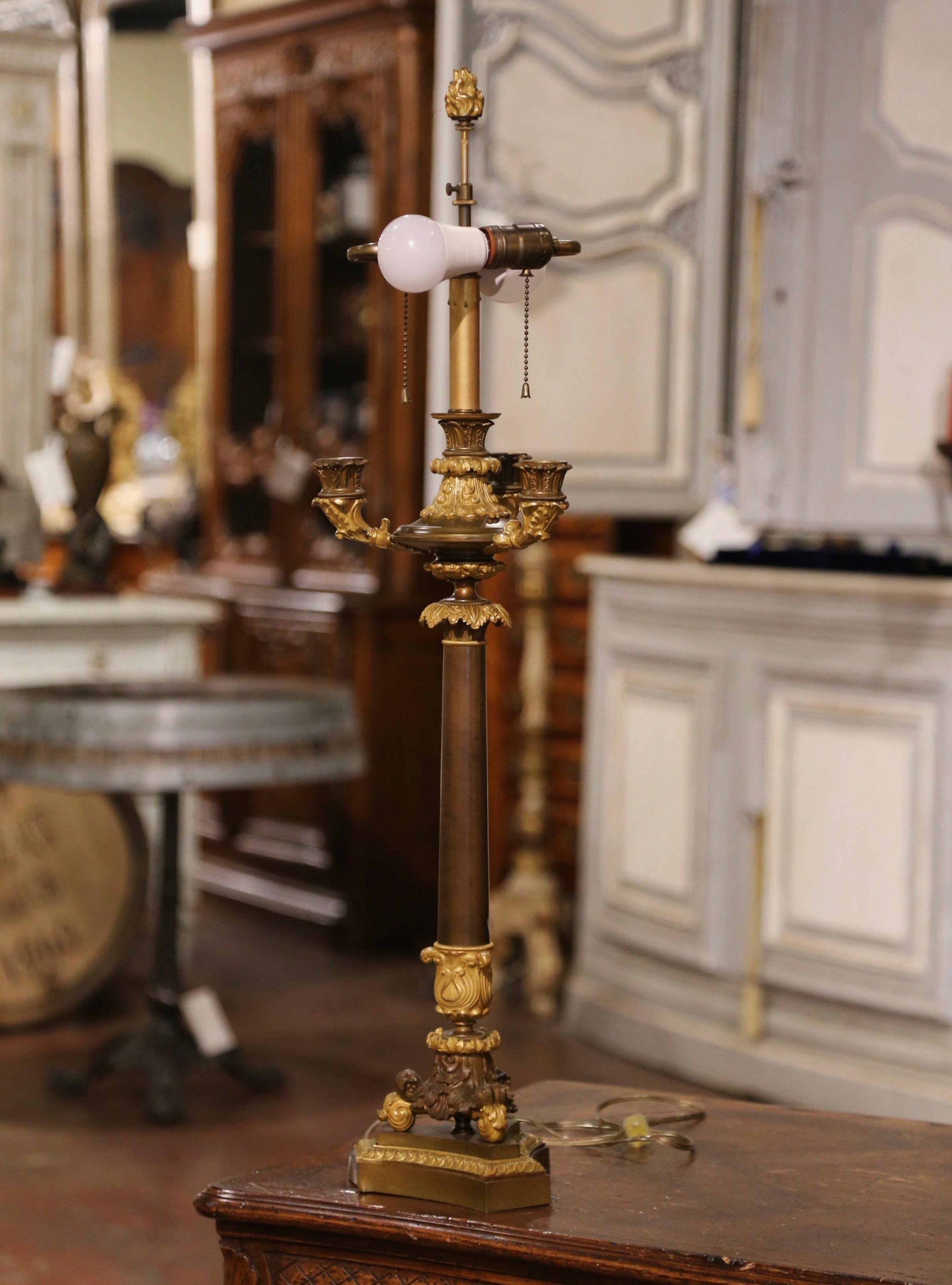 Decorate a desk or library with this elegant antique three-arm candelabra converted into a table lamp. Created in France, circa 1860, the fixture sits on a triangle base embellished with scroll feet and acanthus leaf motif. The top is decorated with