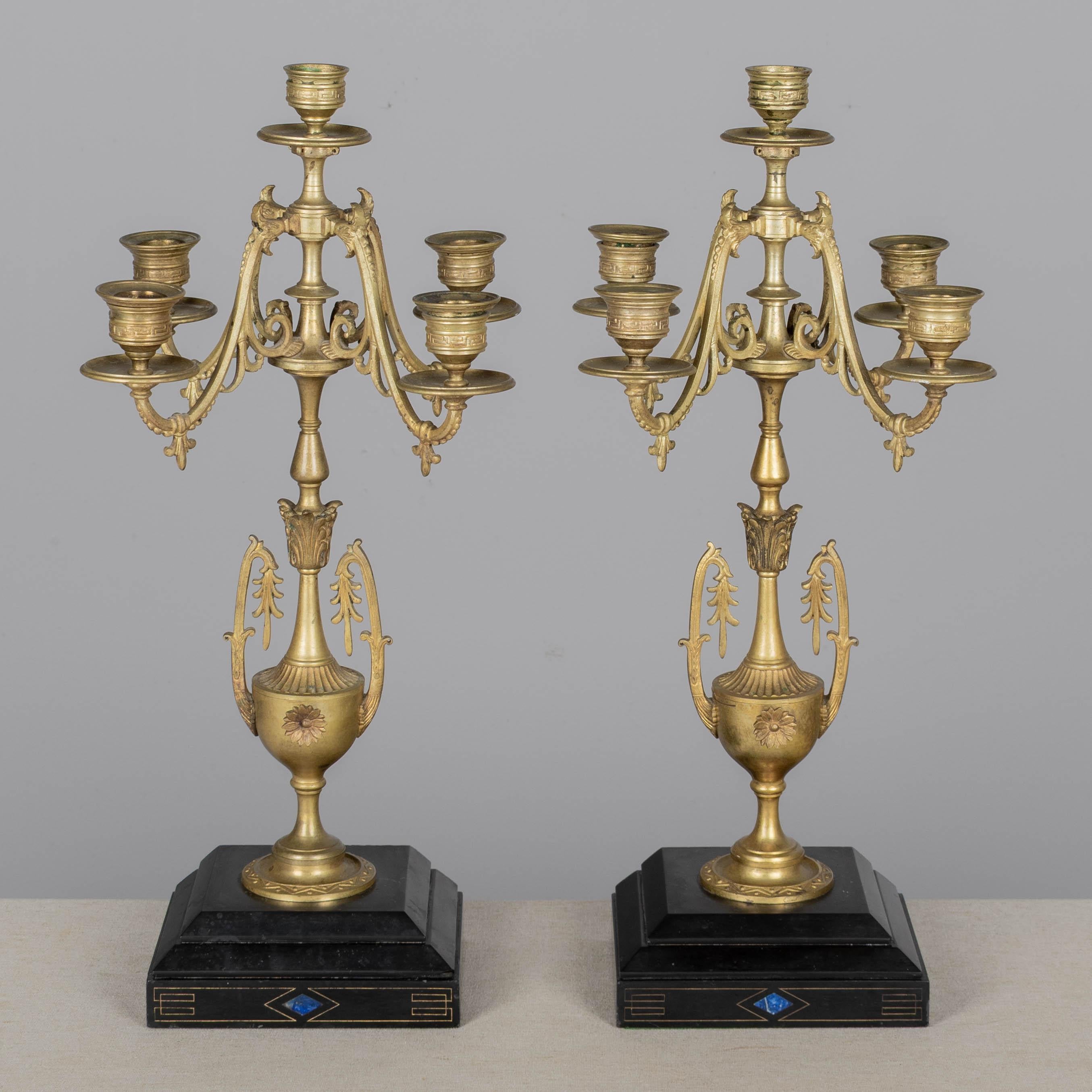 Coppia di candelabri a cinque luci in ottone fuso in stile Impero francese del XIX secolo, ciascuno con base in marmo nero intarsiata con Lapislazzuli. Raffinata fusione con forma a urna, bracci a voluta con dettagli a forma di farina di lisi e