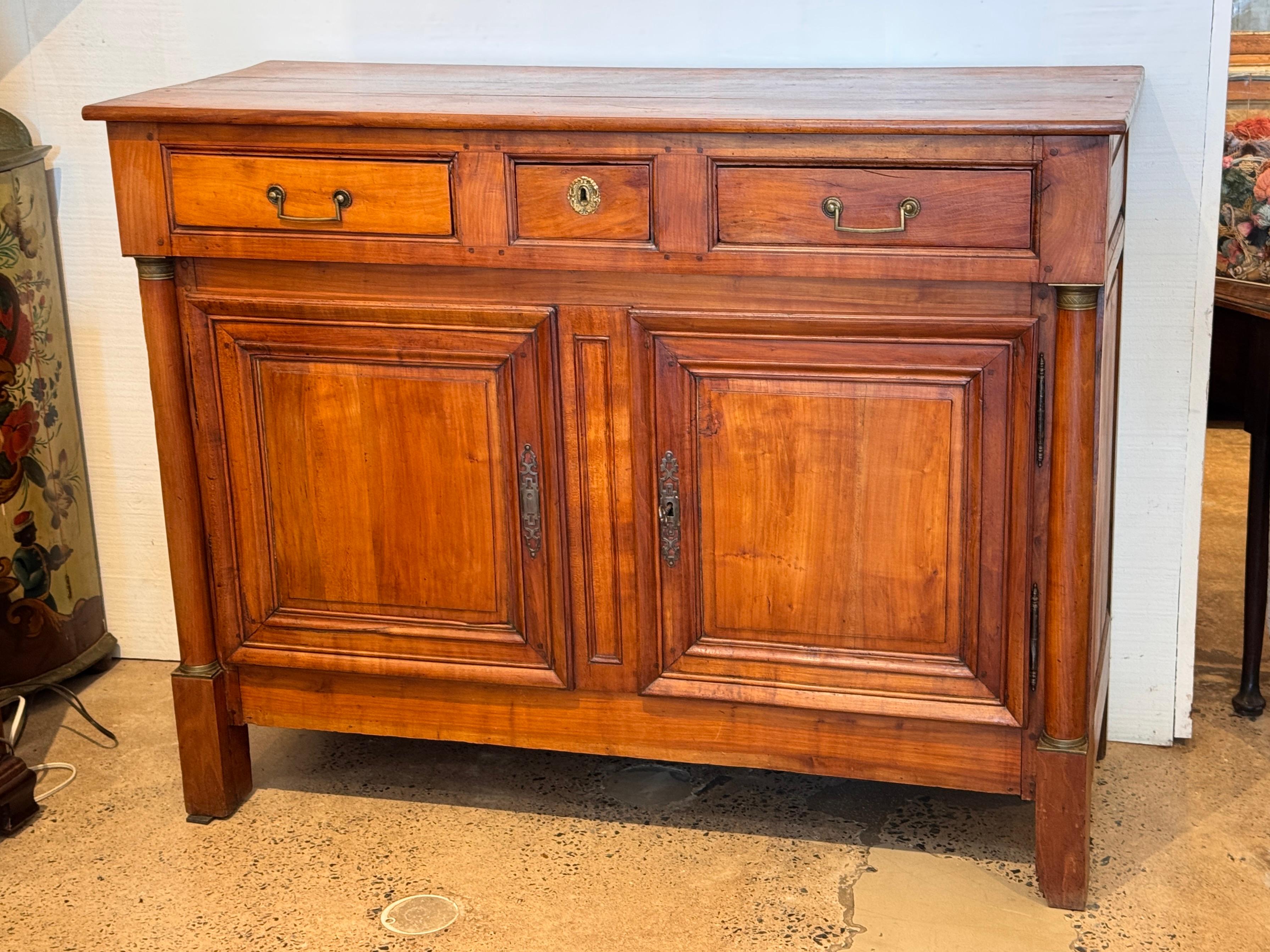 Un buffet Impero francese del XIX secolo realizzato in ciliegio con linee architettoniche classiche e ornamenti sobri. Le caratteristiche includono tre cassetti a coda di rondine sopra due ante a pannello con ferramenta originale in ottone e sottili