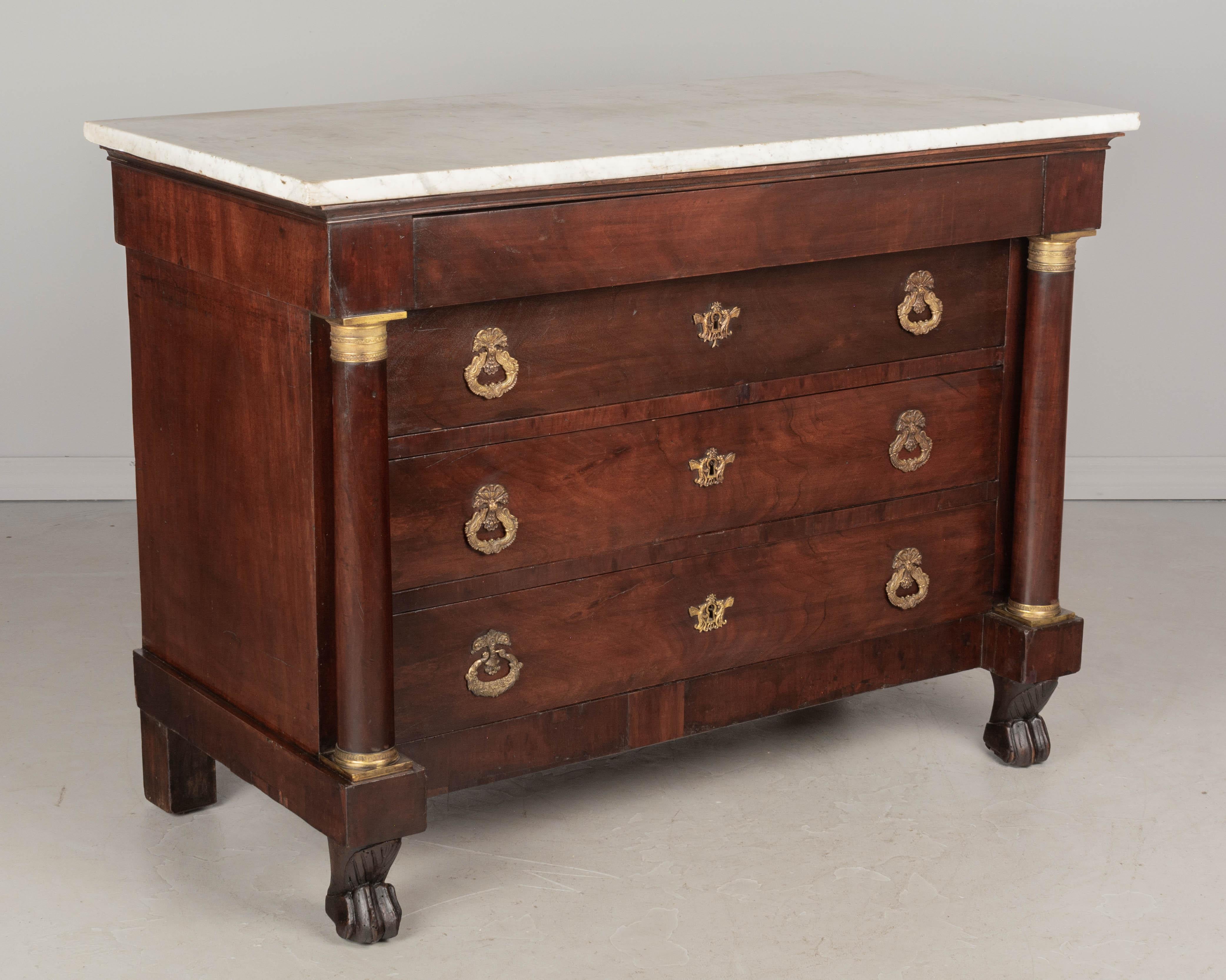 A 19th Century French Empire style commode, or chest of drawers, made of solid and veneer of mahogany. Four dovetailed drawers: three with decorative cast brass pulls and escutcheons, above one slim hidden drawer. Locks are present but there are no