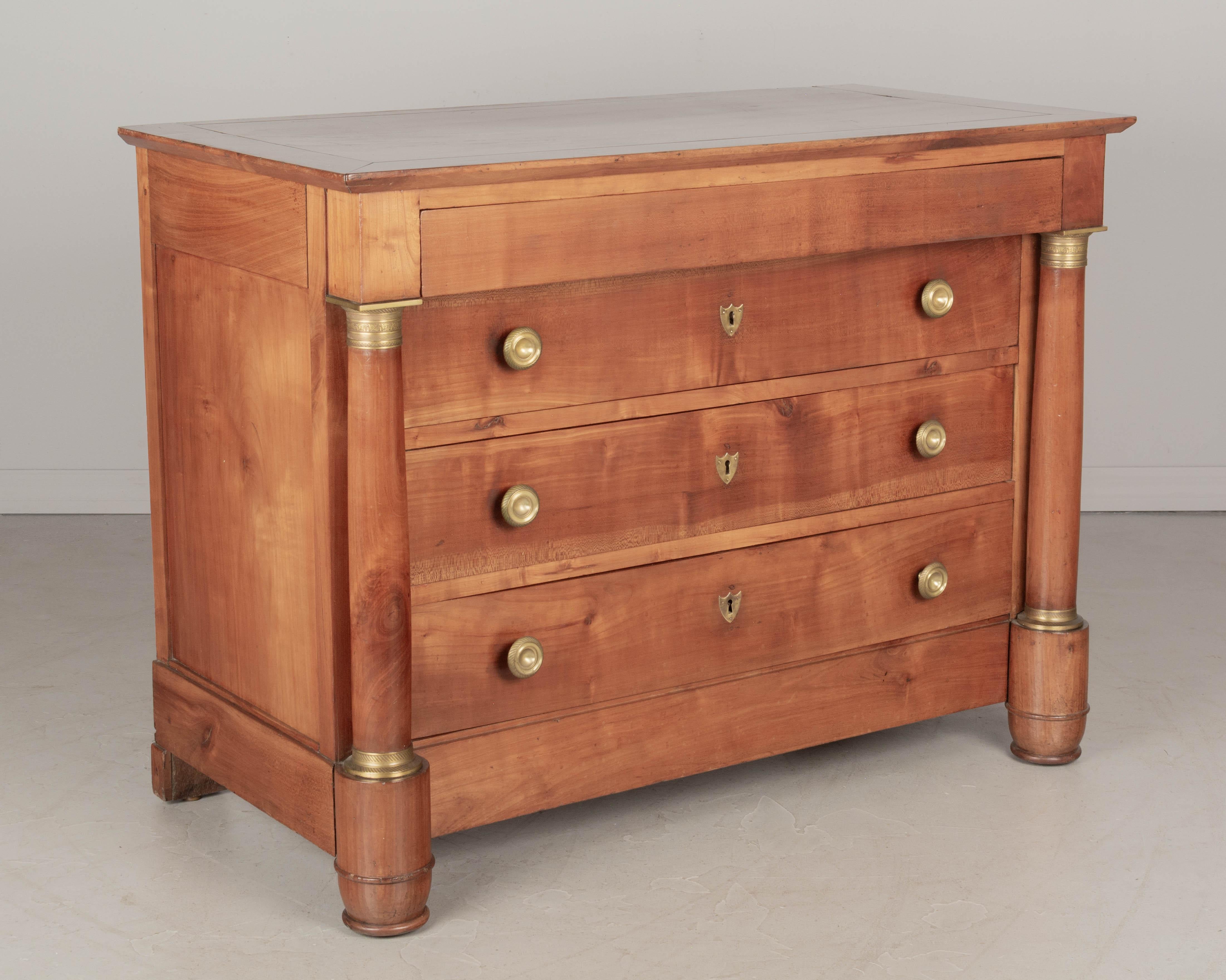 A 19th Century French Empire Period commode from Normandy made of solid cherry wood. Three dovetailed drawers with brass knobs and one hidden top drawer. Large brass mounted turned columns. Exceptional craftsmanship using mortise and tenon add