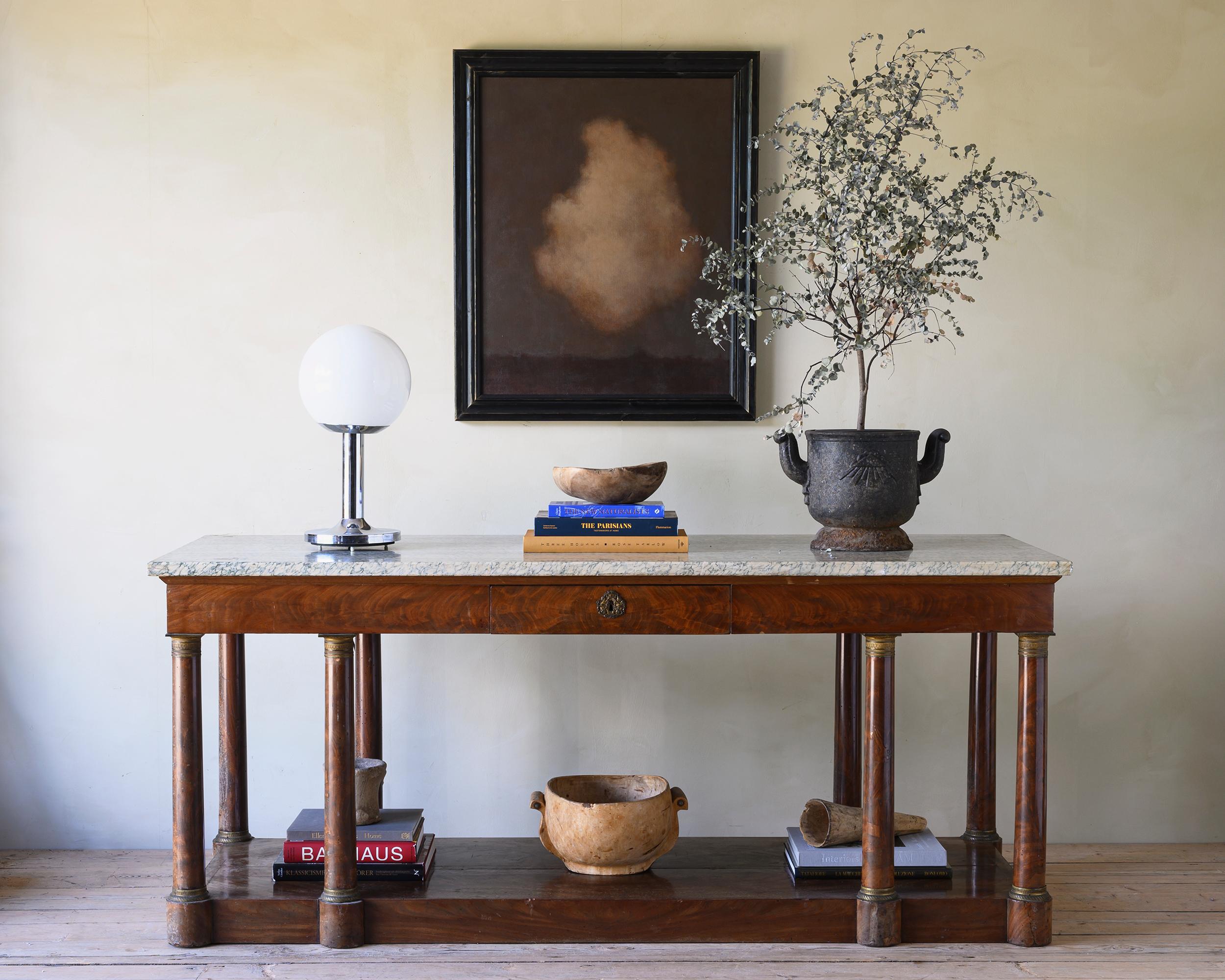 Remarkable and unusually wide French marble topped, mahogany console table from the 19th century. One drawer to the front and two pull out trays on each side. The table is supported by traditional Empire style column legs with ormolu capitals and