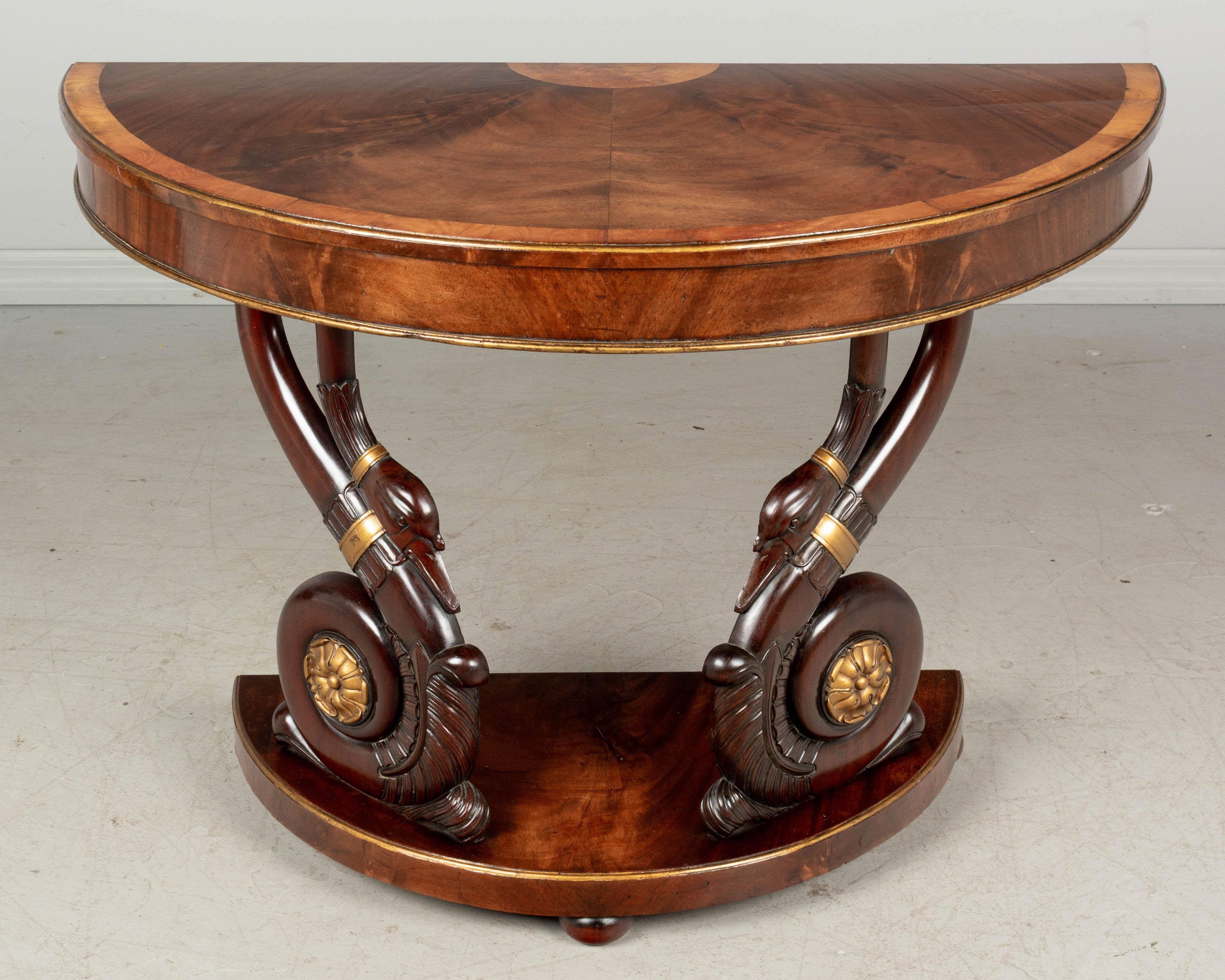 A French Empire demilune console table with a pair of large hand-carved mahogany swans. Good craftsmanship and beautiful stylized sculptural swans with smooth finish and gilt painted accents. Top and base made of veneer of mahogany with book matched
