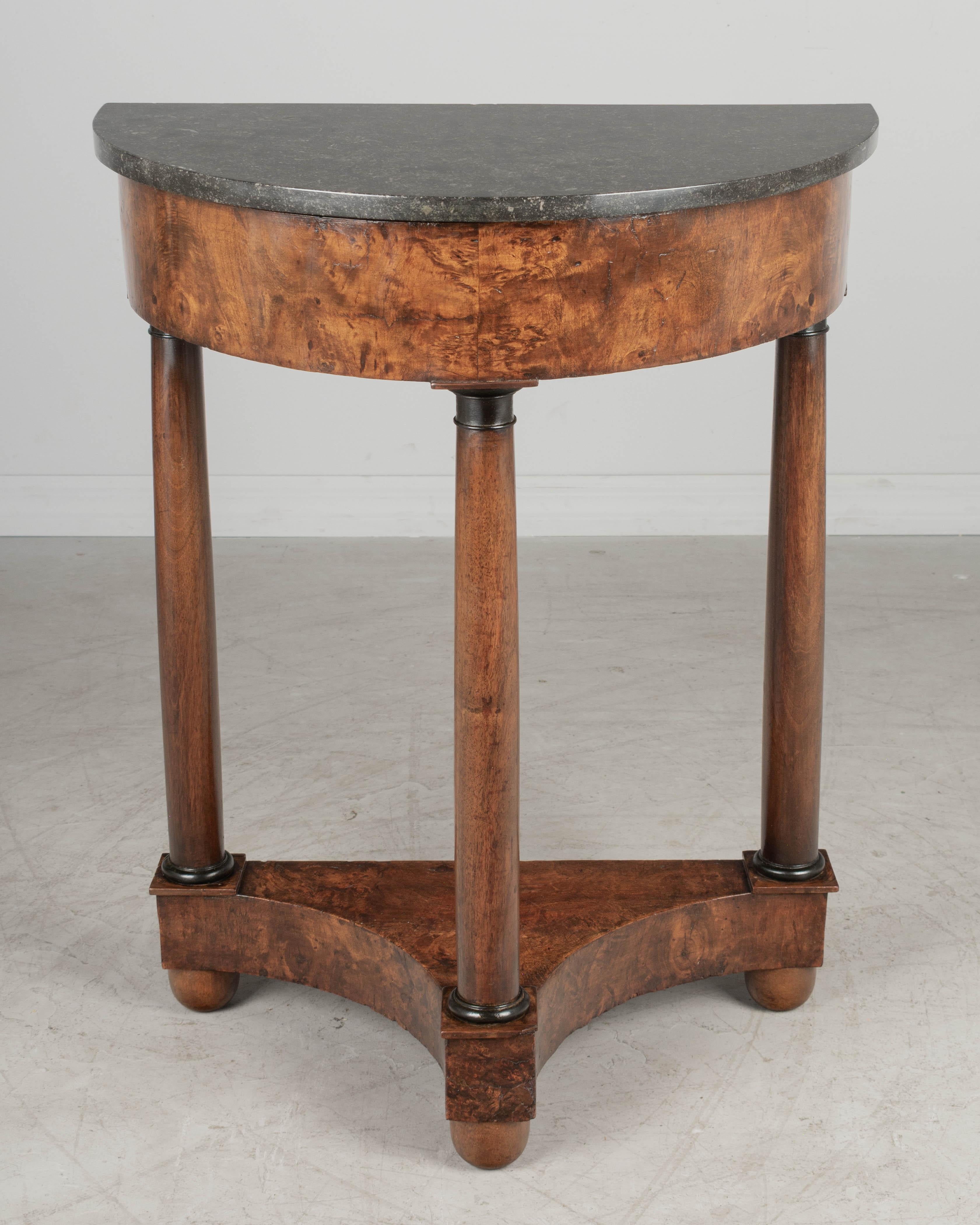 An early 19th century French Empire demilune console table with black marble top. Made of solid walnut with veneer of burled walnut. Turned columns with ebonized capitals. Good craftsmanship. All in good condition. Circa 1820-1840. Turned ball feet
