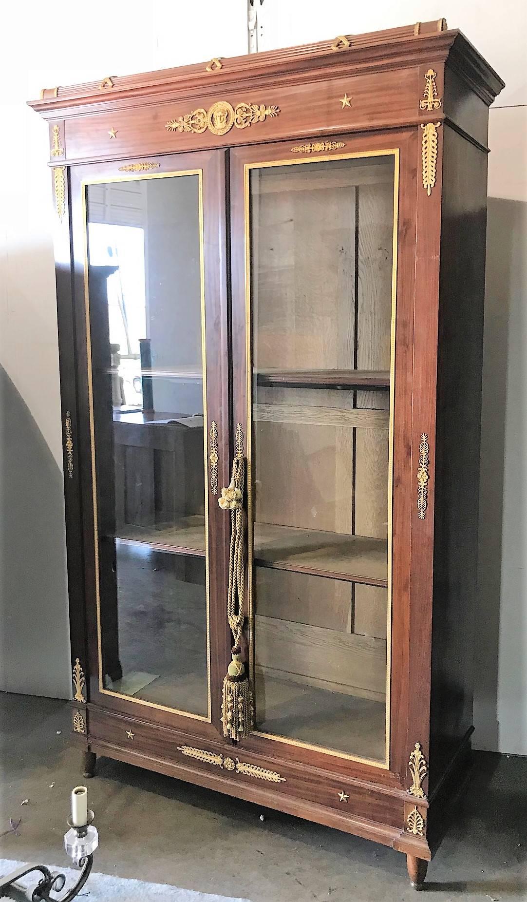 Particularly fine quality 19th century French Empire mahogany display cabinet or bibliotheque/bookcase with two large glass fronted doors trimmed in doré bronze and fitted with interior shelves. Appointed with exquisite and finely detailed gold