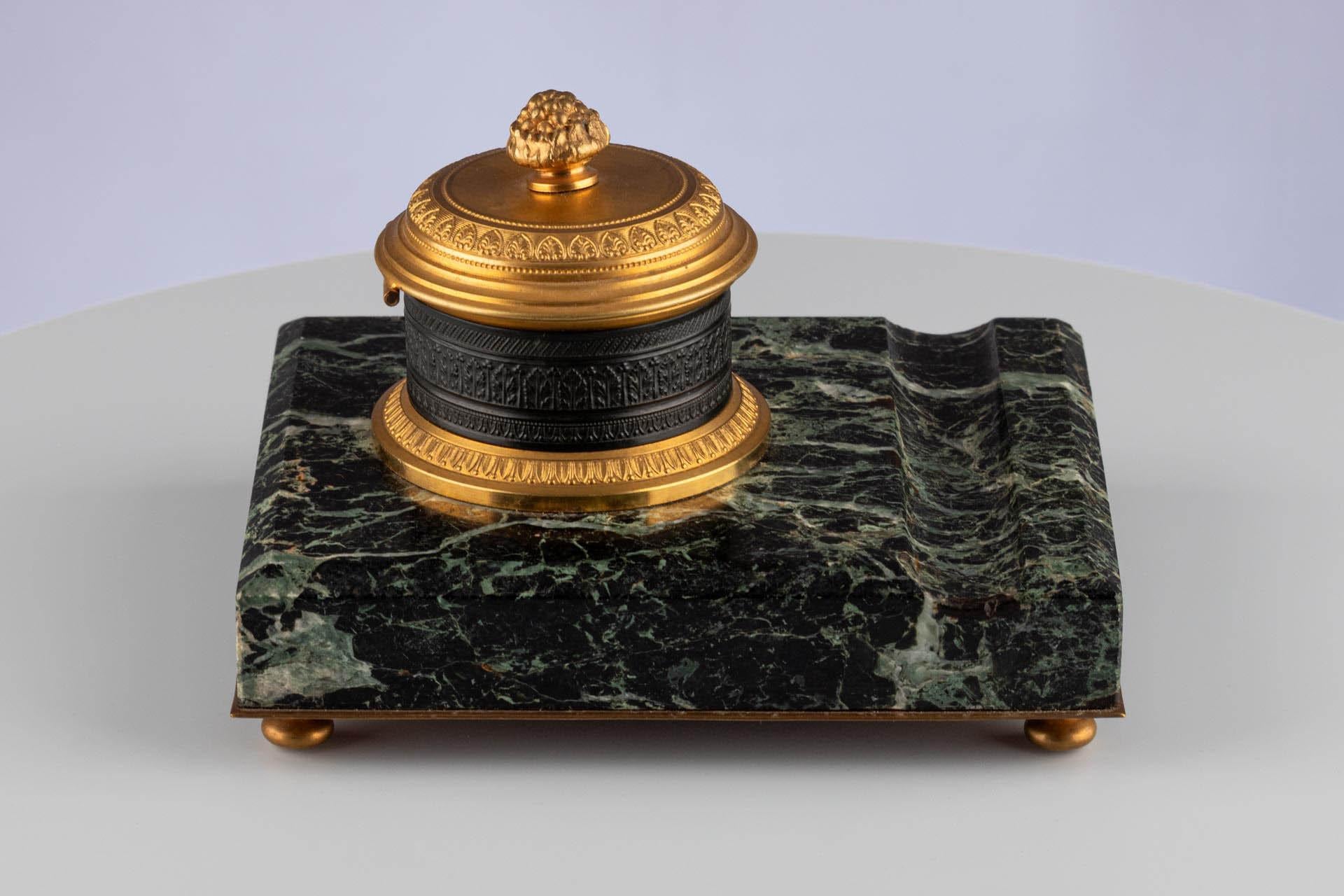 Calamaio con montatura in bronzo e base in marmo

Origine: Francia
Materiale: Bronzo dorato e patinato, marmo verde
Data: Secondo Impero, circa 1860-1880

Dimensioni:
H. H. × L. × P.: 10 × 13 × 16 cm.

Descrizione:
Questo elegante calamaio poggia su