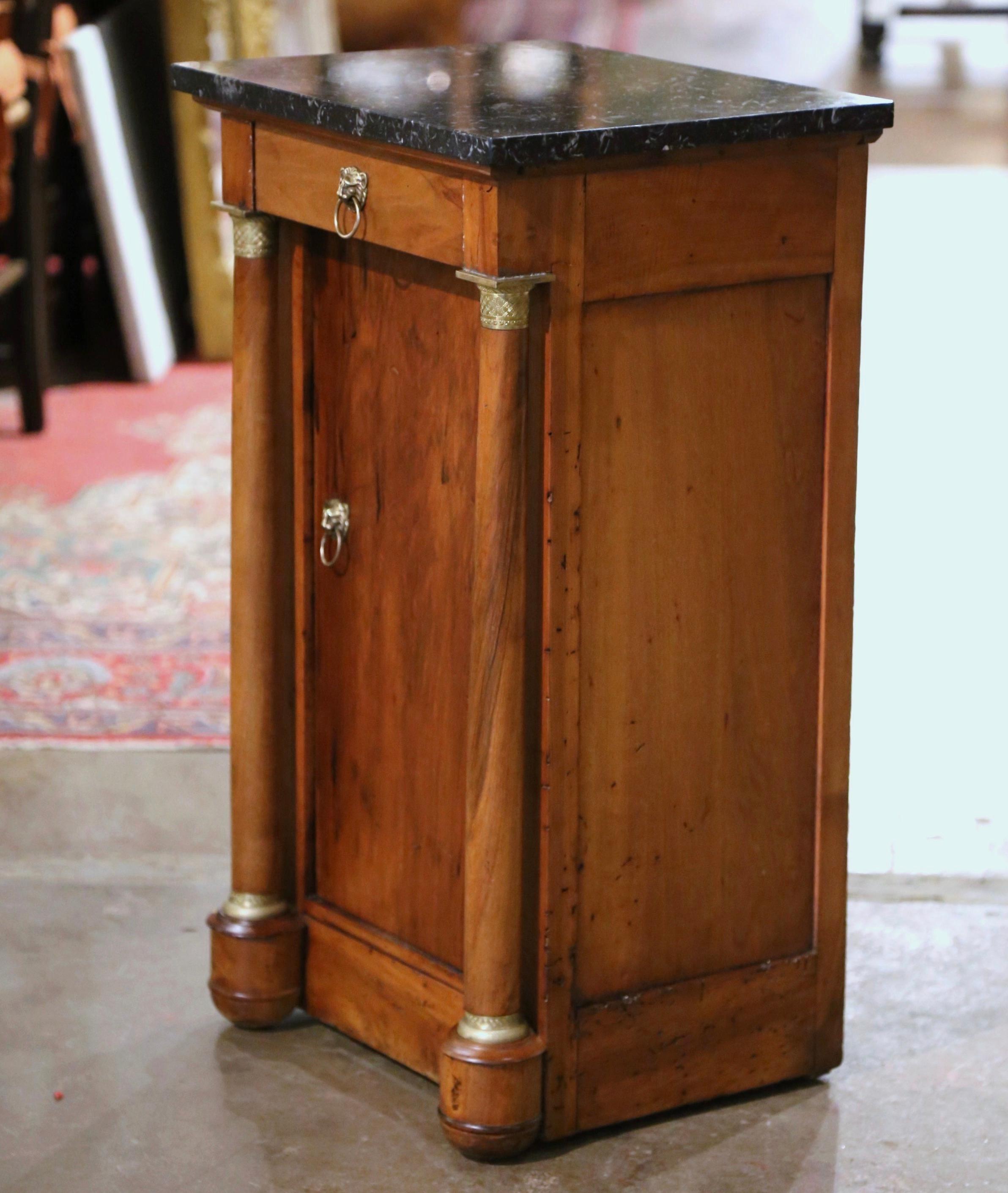 Crafted in France, circa 1870, the elegant antique cabinet is decorated with front rounded columns ending with bun feet, and embellished with decorative brass mounts at the shoulder and the base. The small fruit wood chest features a drawer across