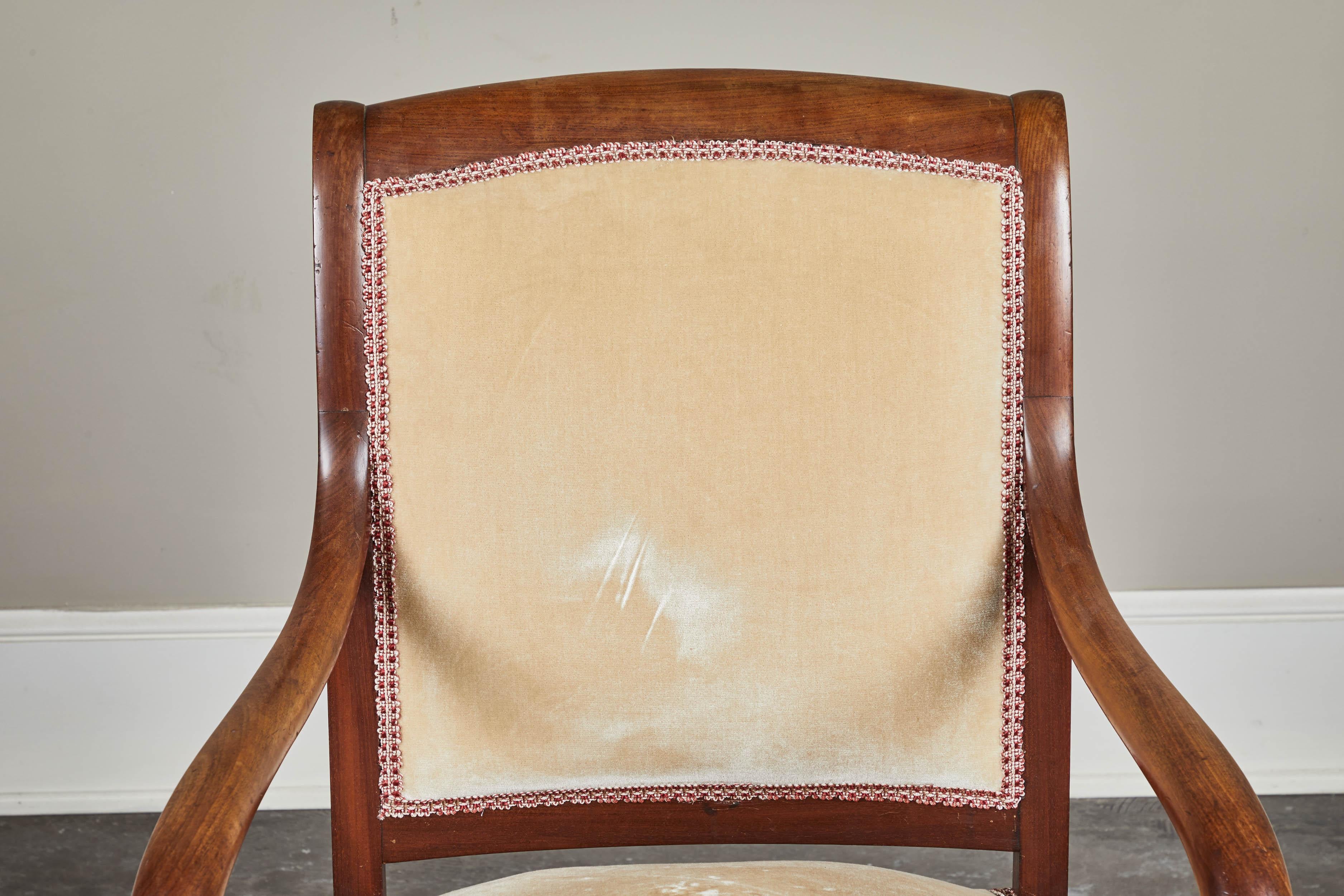 A lovely 19th century French mahogany empire armchair featuring a curved back crest, scrolled arms and shaped legs. The back is fully upholstered.