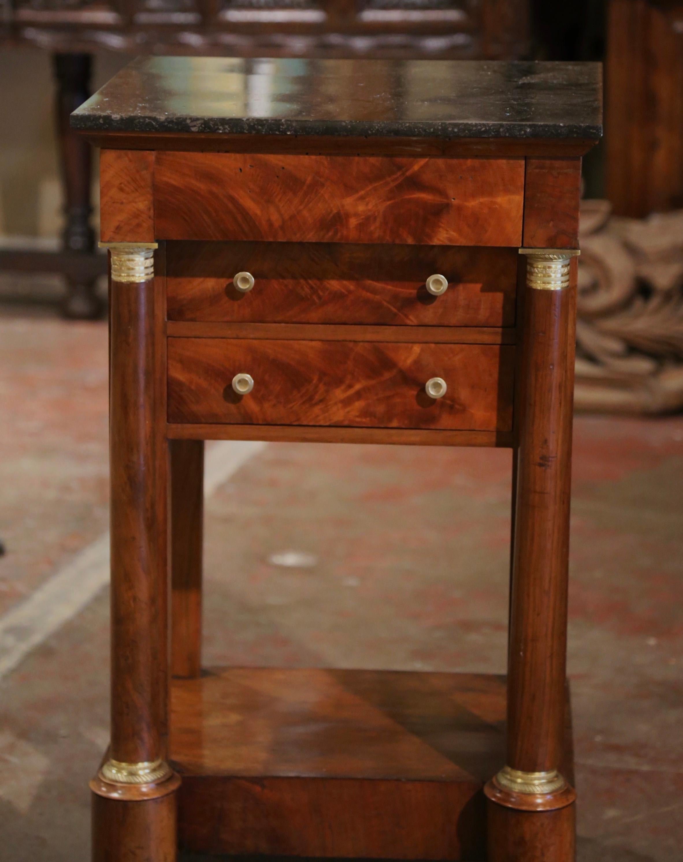 Crafted in France circa 1850 and built of mahogany, the elegant antique cabinet stands on front rounded columns ending with bun feet and embellished with decorative bronze mounted rings at the shoulder and the base. The small chest features three