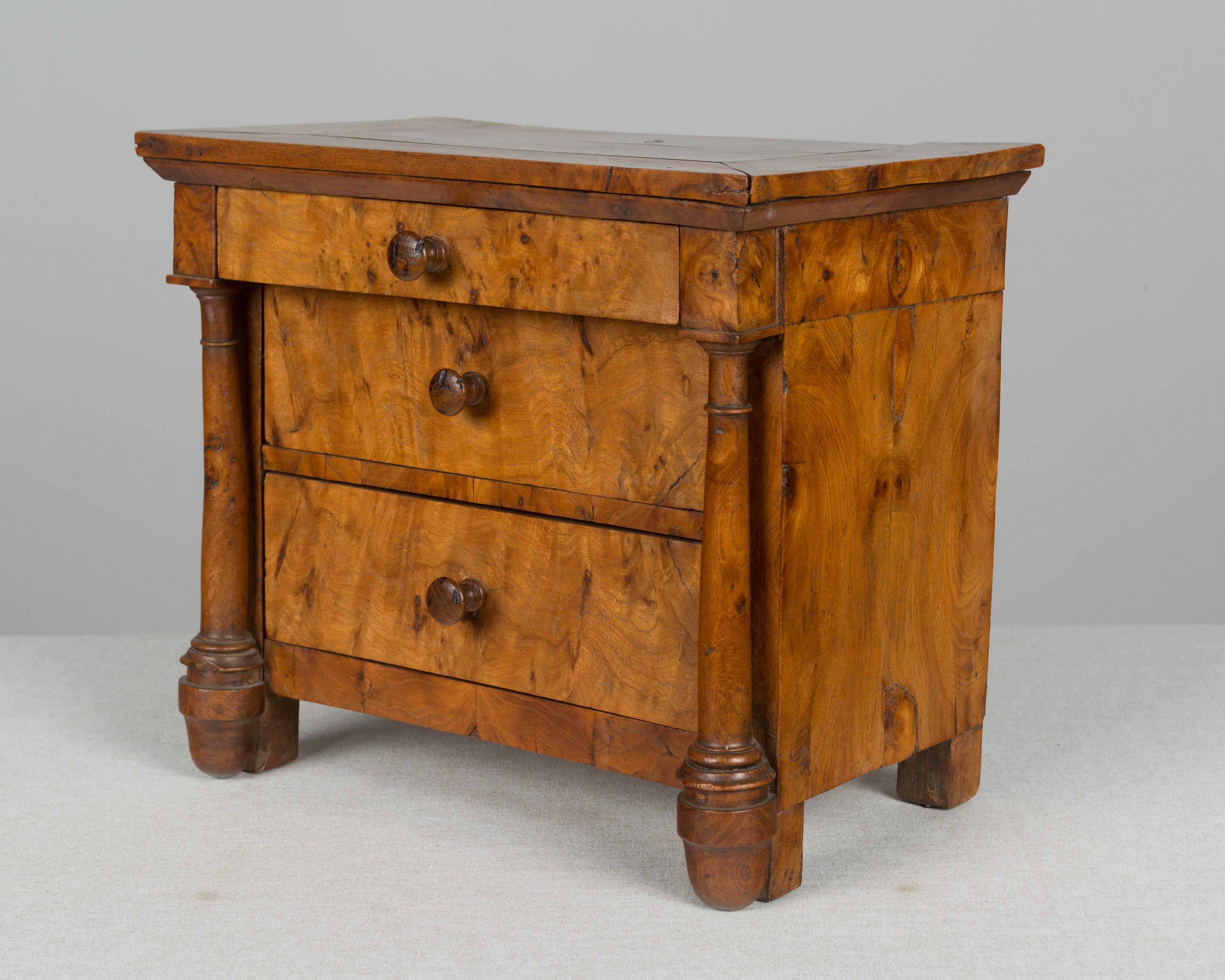 A 19th century French Empire miniature commode. A well executed miniature chest made of walnut and veneer of walnut with two large drawers below a smaller top drawer and with solid walnut columns. Inscription written in ink on the back of each of