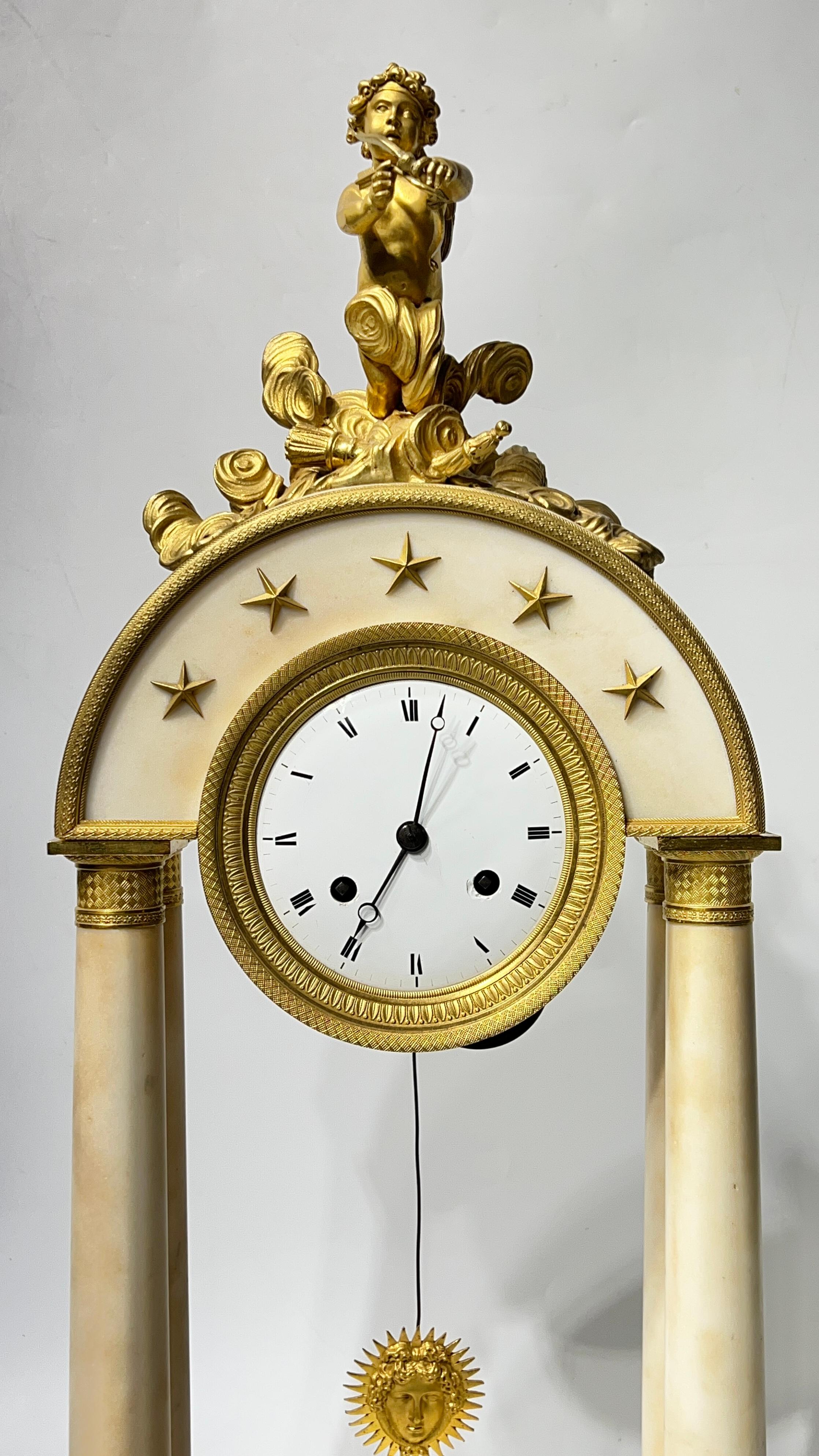 Bellissimo orologio da camino francese a forma di portico del XIX secolo in marmo bianco con montature in bronzo ormolu finemente fuse, che si distingue per le sue grandi dimensioni e per il Cupido con arco tra le nuvole nella parte superiore. 