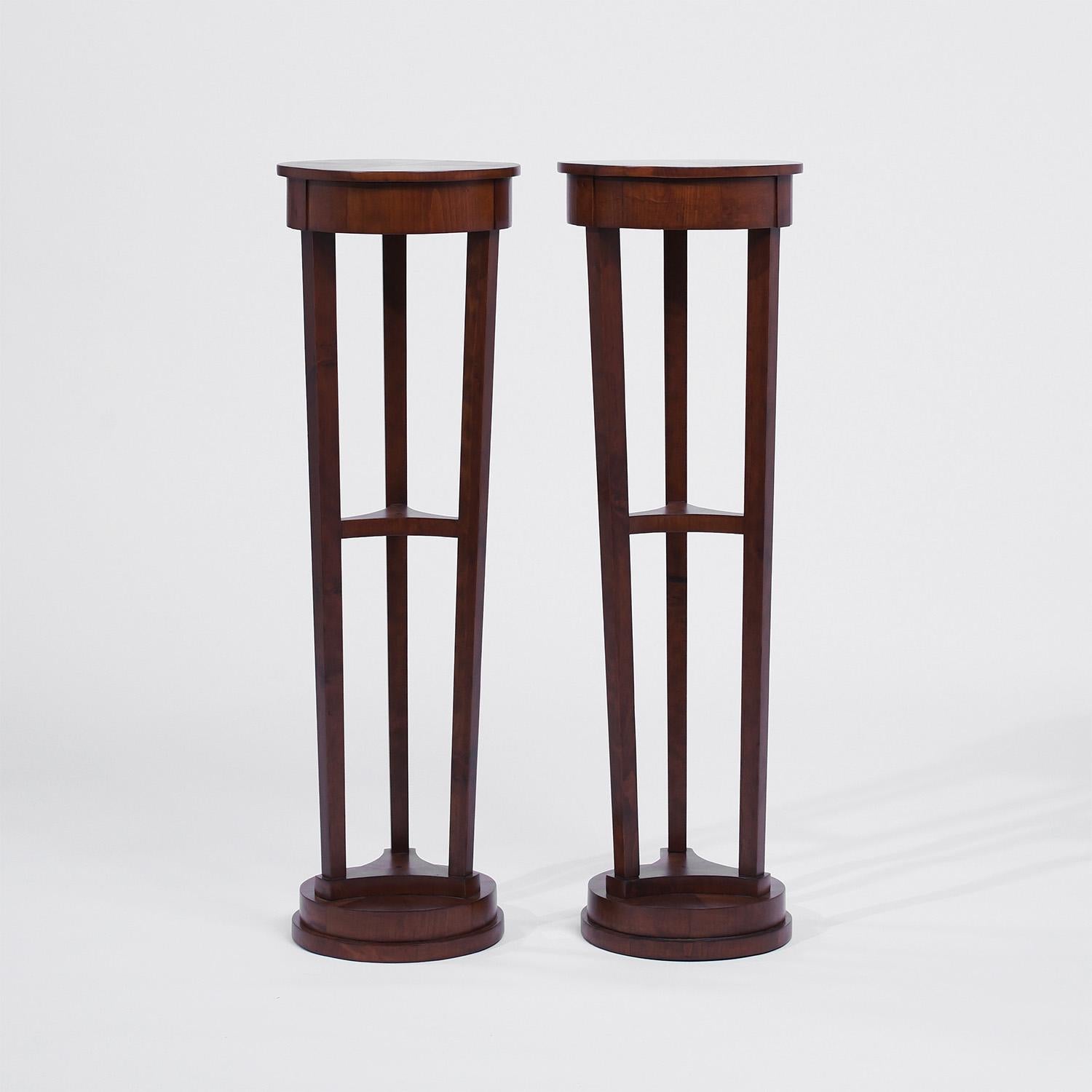 Paire de guéridons anciens en acajou travaillés à la main, en bon état. Chacun des podiums polis à la gomme-laque parisienne est composé d'une petite étagère centrale, rehaussée par des sculptures en bois détaillées. Les pièces du décor du salon