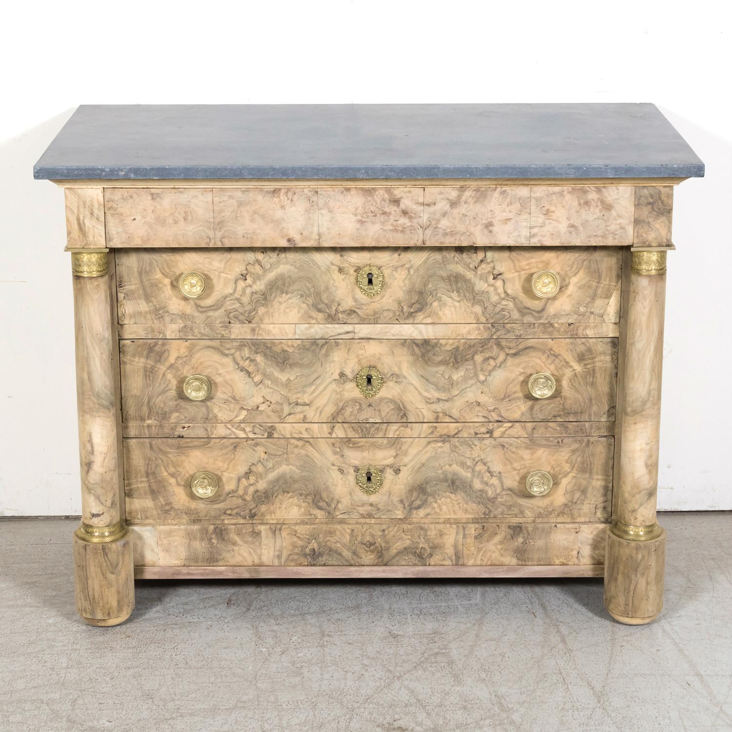 A fine 19th century French Empire period four-drawer commode handcrafted of walnut, circa 1810. Having a bleached finish, this handsome antique French chest of drawers features a bookmatched burled walnut front with a gray fossil marble top resting