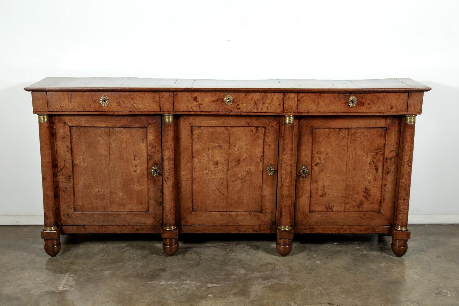 A very fine early 19th century French period Empire enfilade buffet handcrafted of burled chestnut near the Ile de France region, having three drawers over three doors flanked by support columns with original gilt-bronze capitals. Each column ending
