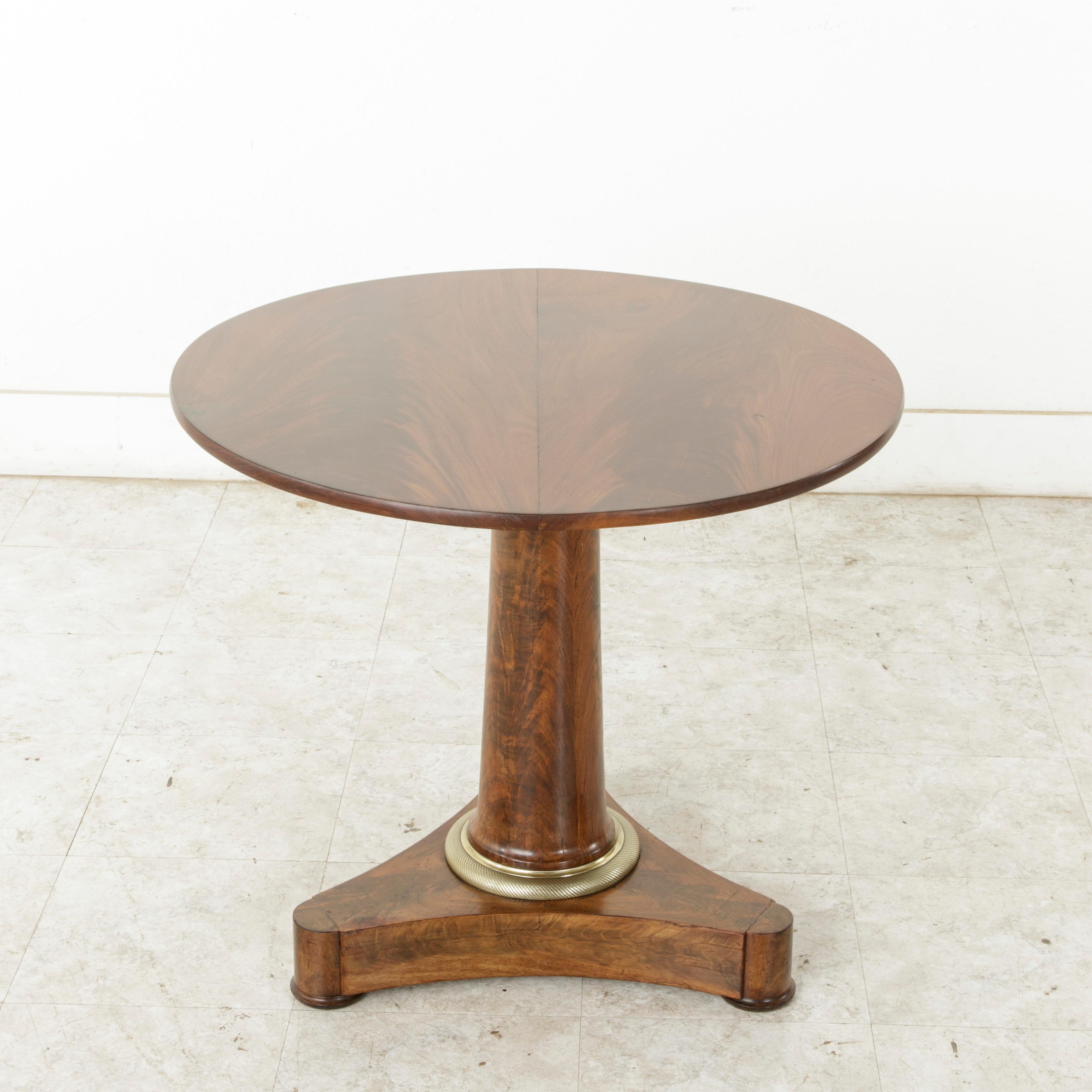 This 19th century French Empire period gueridon or pedestal table is constructed of solid mahogany. Its mahogany top is formed with two planks of wood resting on a central pillar. A chiseled bronze ring detailed with beading surrounds the bottom of