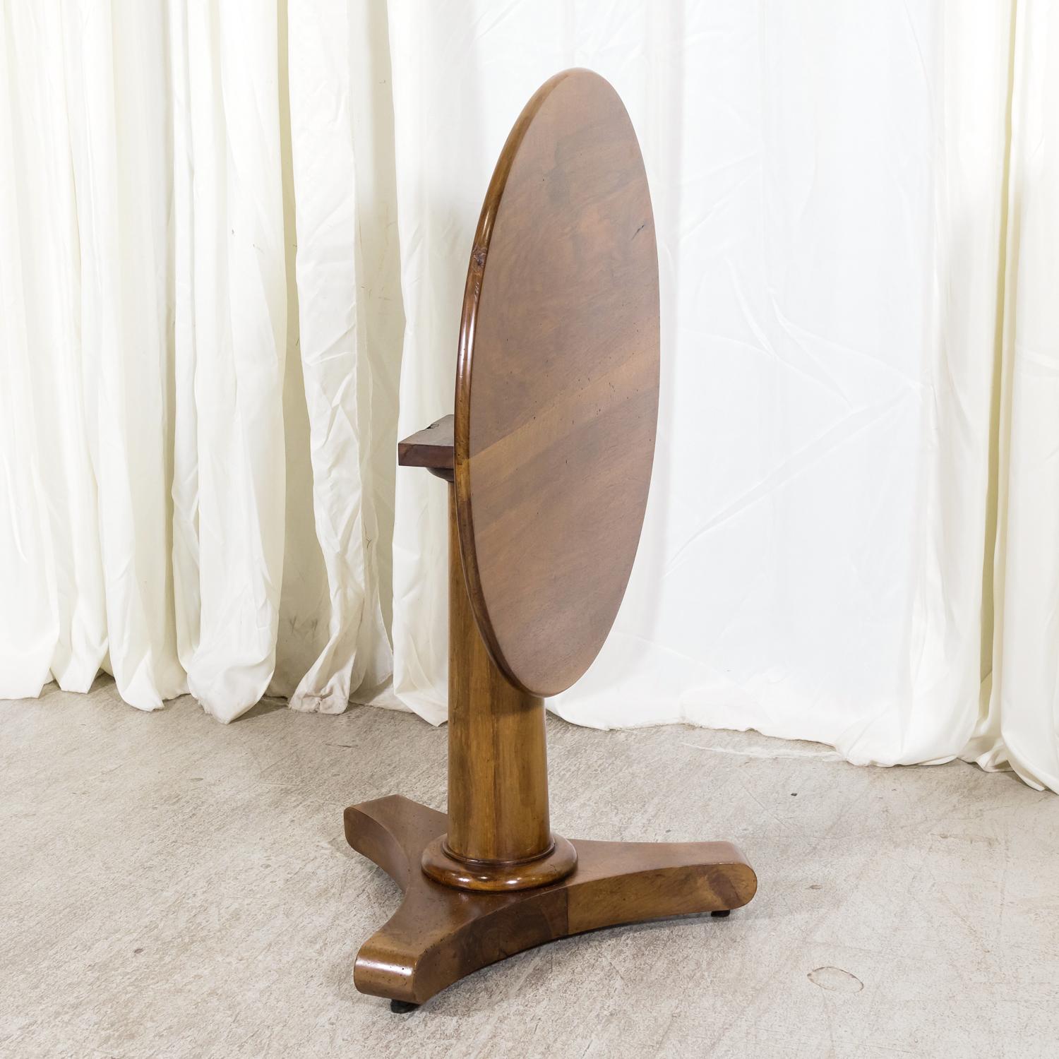 A handsome 19th century French Empire period tilt top gueridon side table or center table handcrafted of solid walnut in the South of France, circa early 1800s. This antique table features a round top raised on a tapered column support and tripod