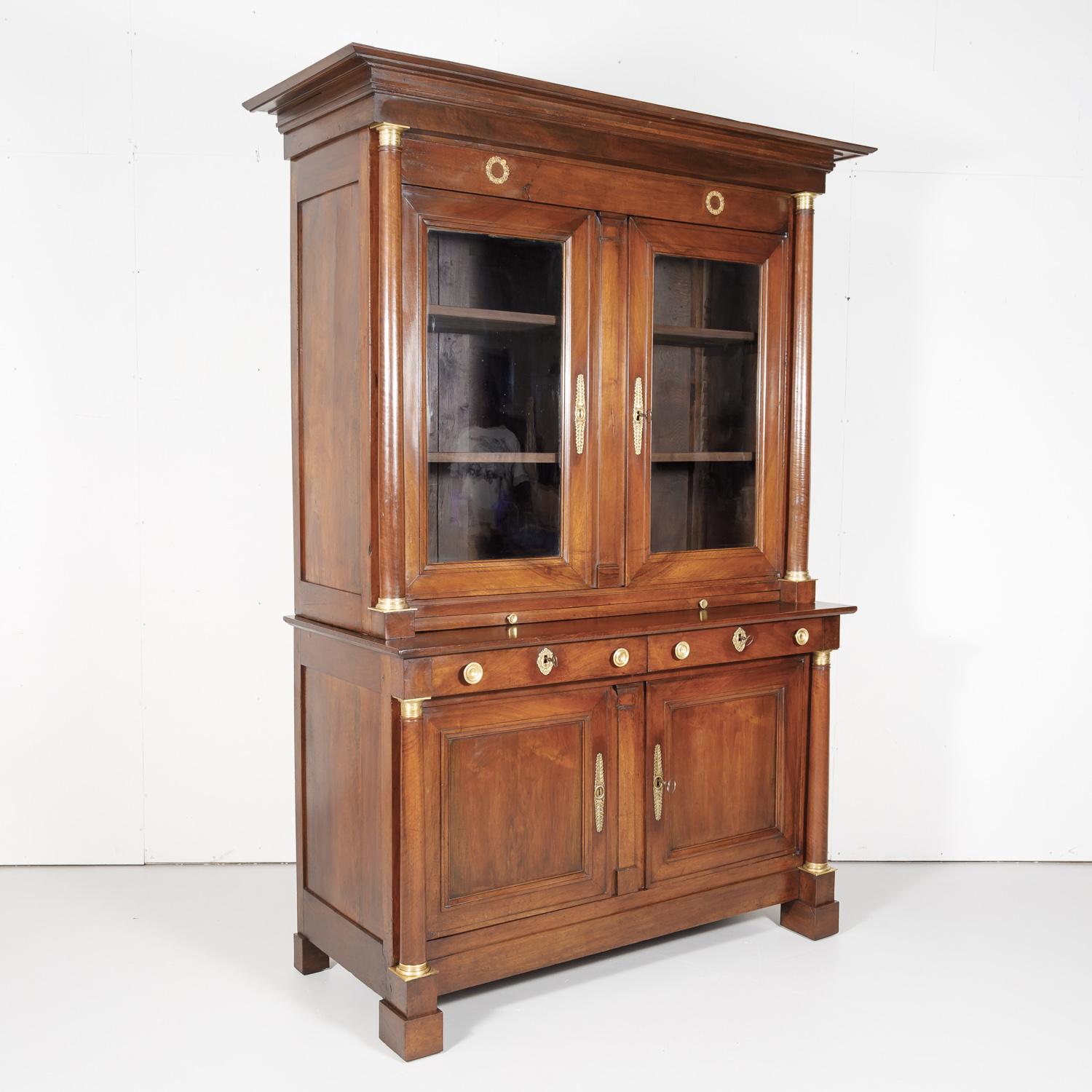 A fine French Empire period bibliotheque handcrafted from select French walnut by skilled artisans from Lyon during the First Empire of Napoleon, circa early 1800s. The upper bookcase of this grand piece boasts a stepped cornice over a frieze with