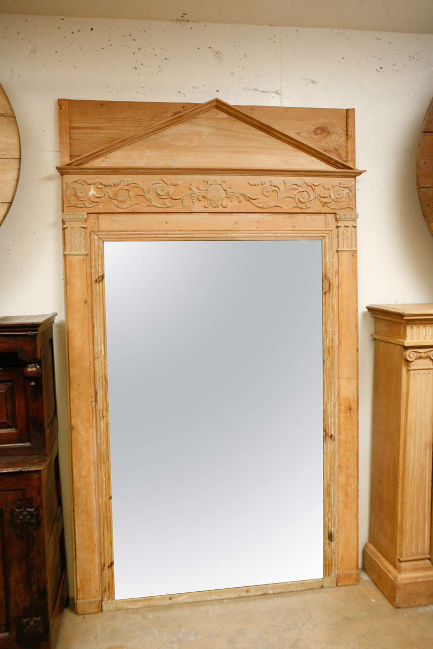 19th-century French Empire style mirror with exquisitely carved naked pine wood frame. The neoclassical flourishes have an architectural theme and include a spare pediment top, frieze with foliate scroll motif, and two lower Corinthian capitol