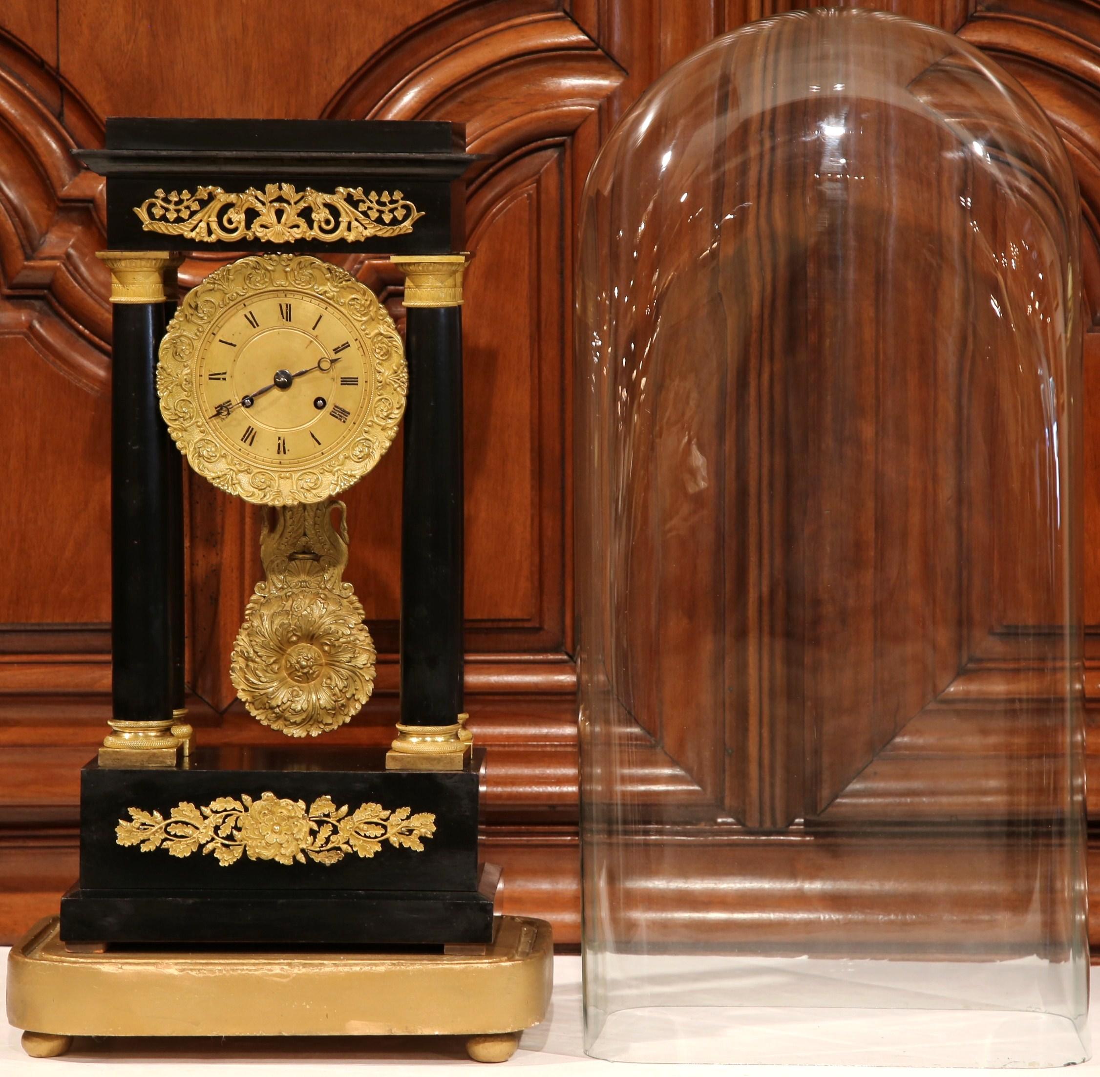 Keep time in your office, study, or atop your mantel with this elegant antique clock in the original glass dome. Crafted in France, circa 1870, the portico clock stands on a wooden gilt base with small bun feet; it features four columnar supports
