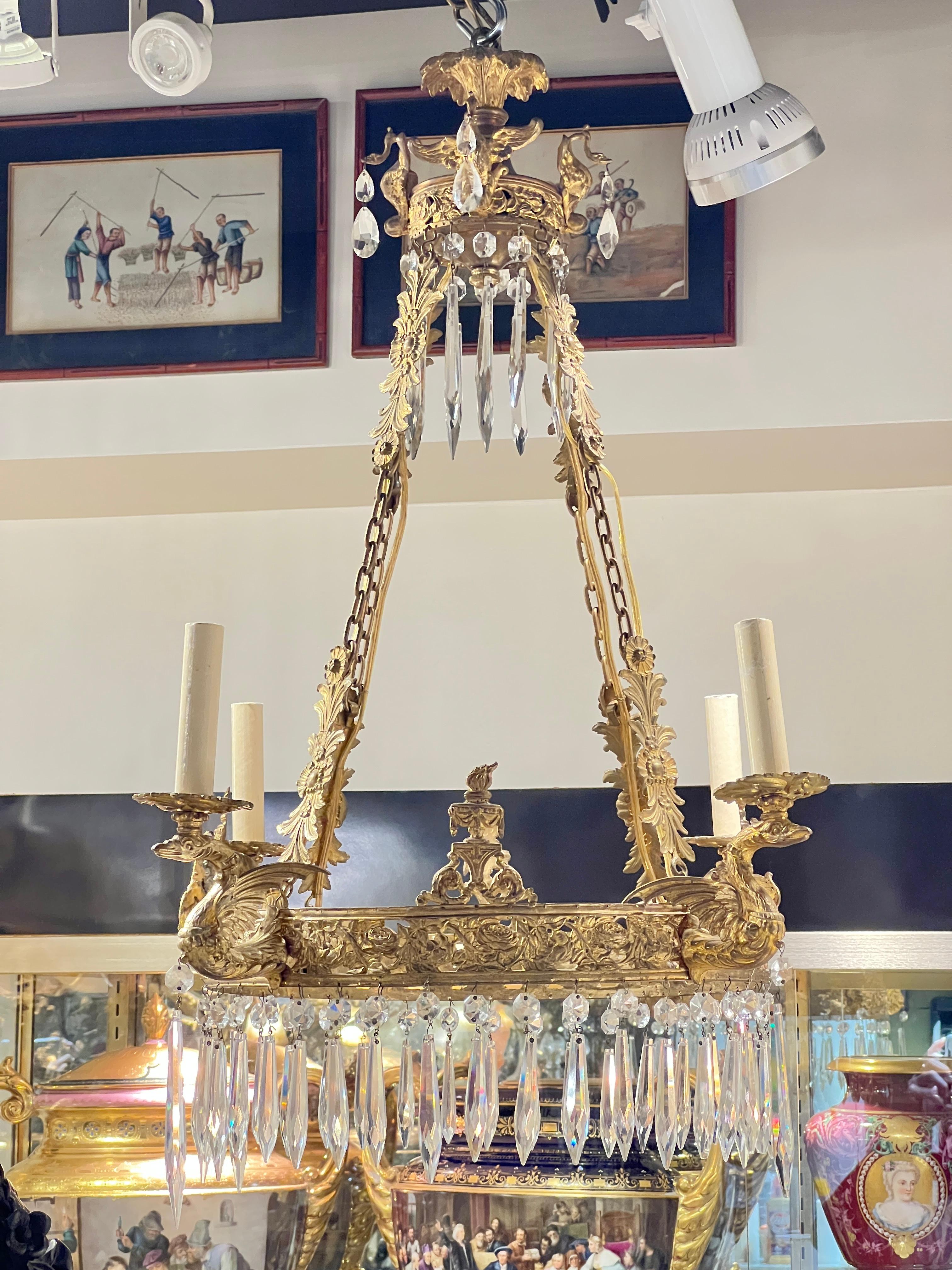 19th century gilt bronze chandelier in the French Empire style with circular form with reticulated designs of rose flowers surmounted with neoclassical torches, and four electrified candle arms rising above griffins, suspended by four chains