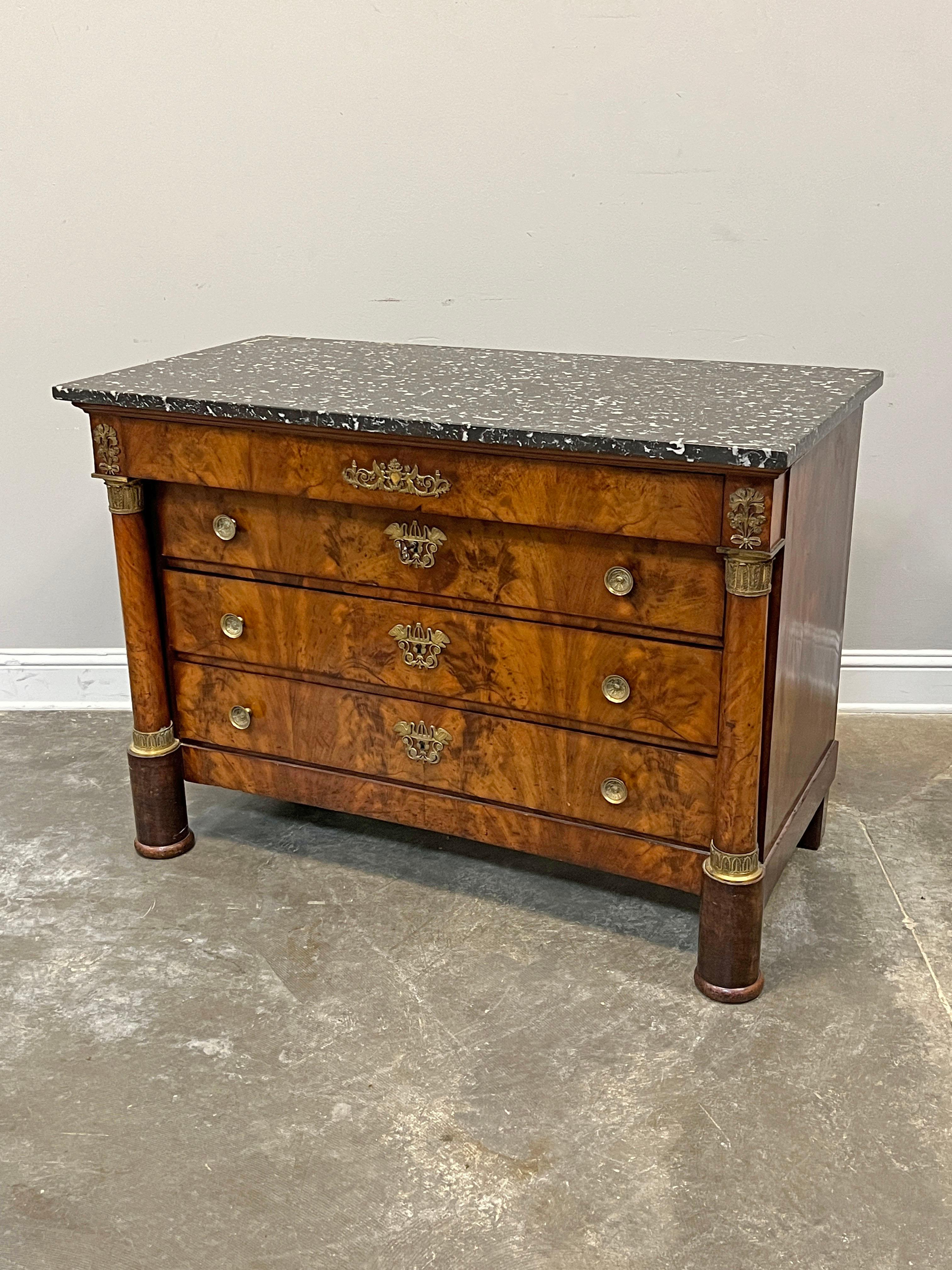 Commode in stile Impero francese del XIX secolo in mogano con piano in marmo. Realizzato con impiallacciatura burattata, il mobile è affiancato da colonne con decorazioni in ottone. Presenta montature e tiranti in ormolu con motivi classici.