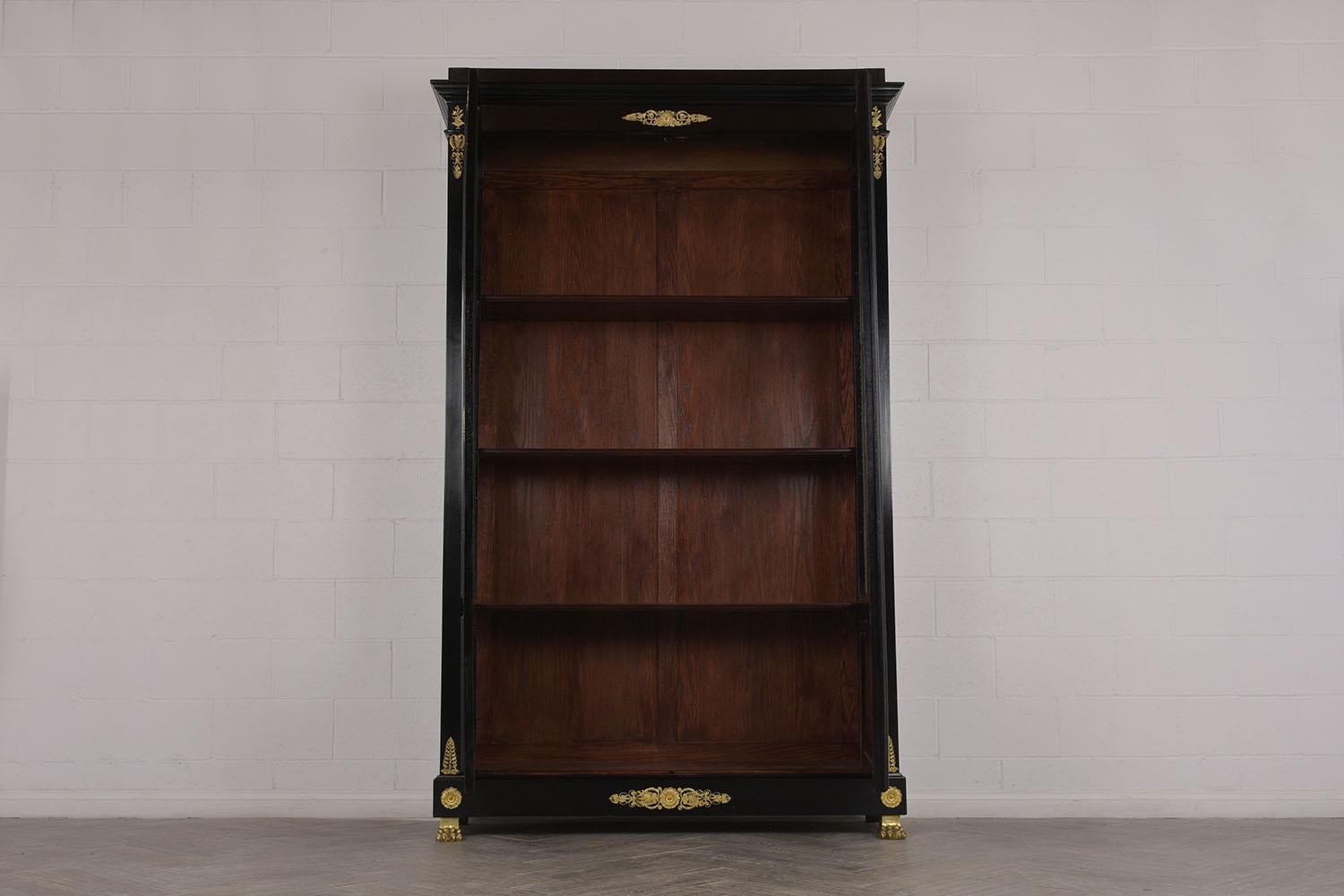 This Late 19th century French Empire Style Bookcase is made out of mahogany wood with a newly ebonized lacquered finish and has been newly restored. The display features elegant brass accents throughout the piece, two doors with its original brass