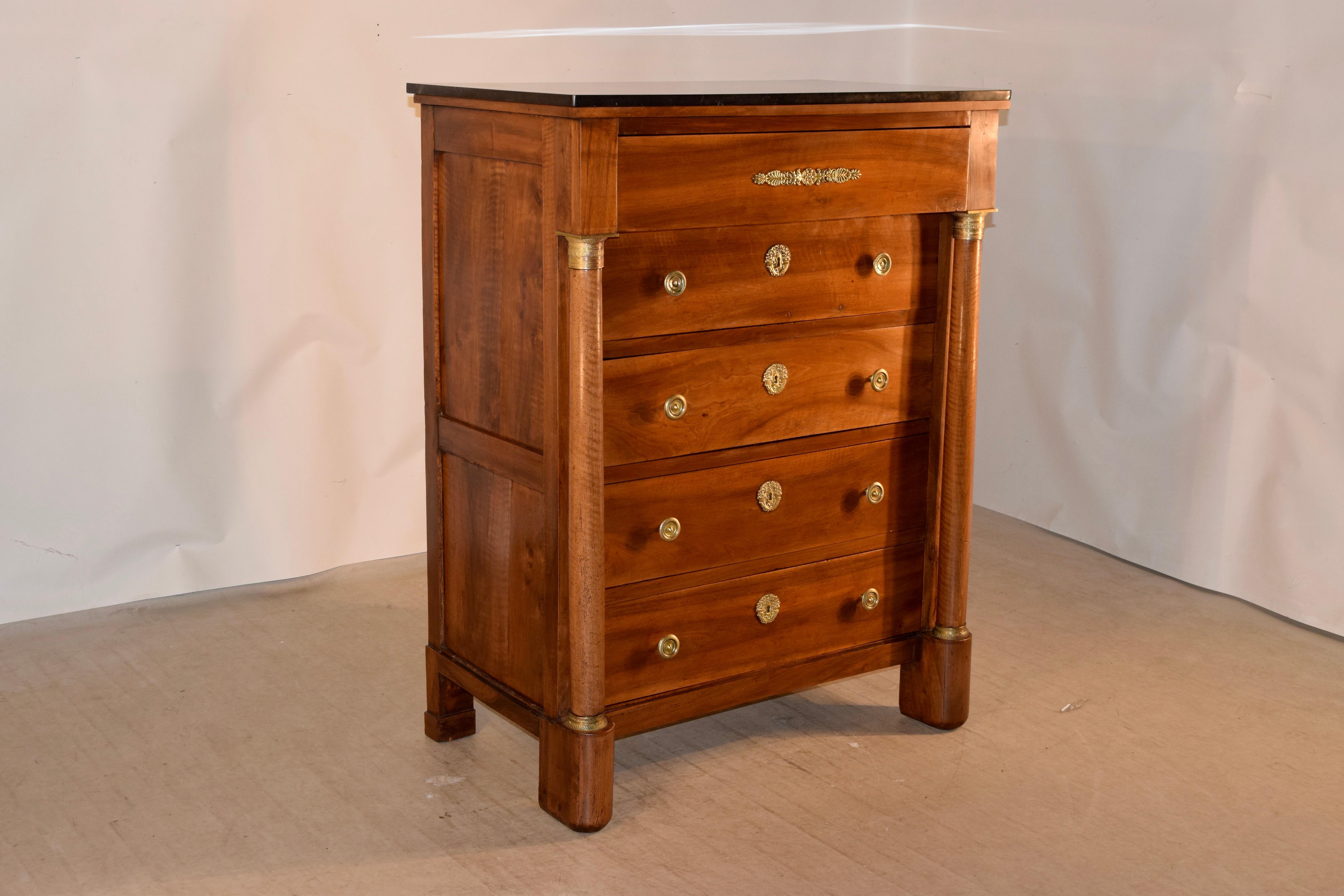 Early 19th century French tall chest of drawers with a black marble top, made from walnut. The case is lovely and has paneled sides and a single upper projecting drawer over four flush drawers. These are flanked by full turned columns and are