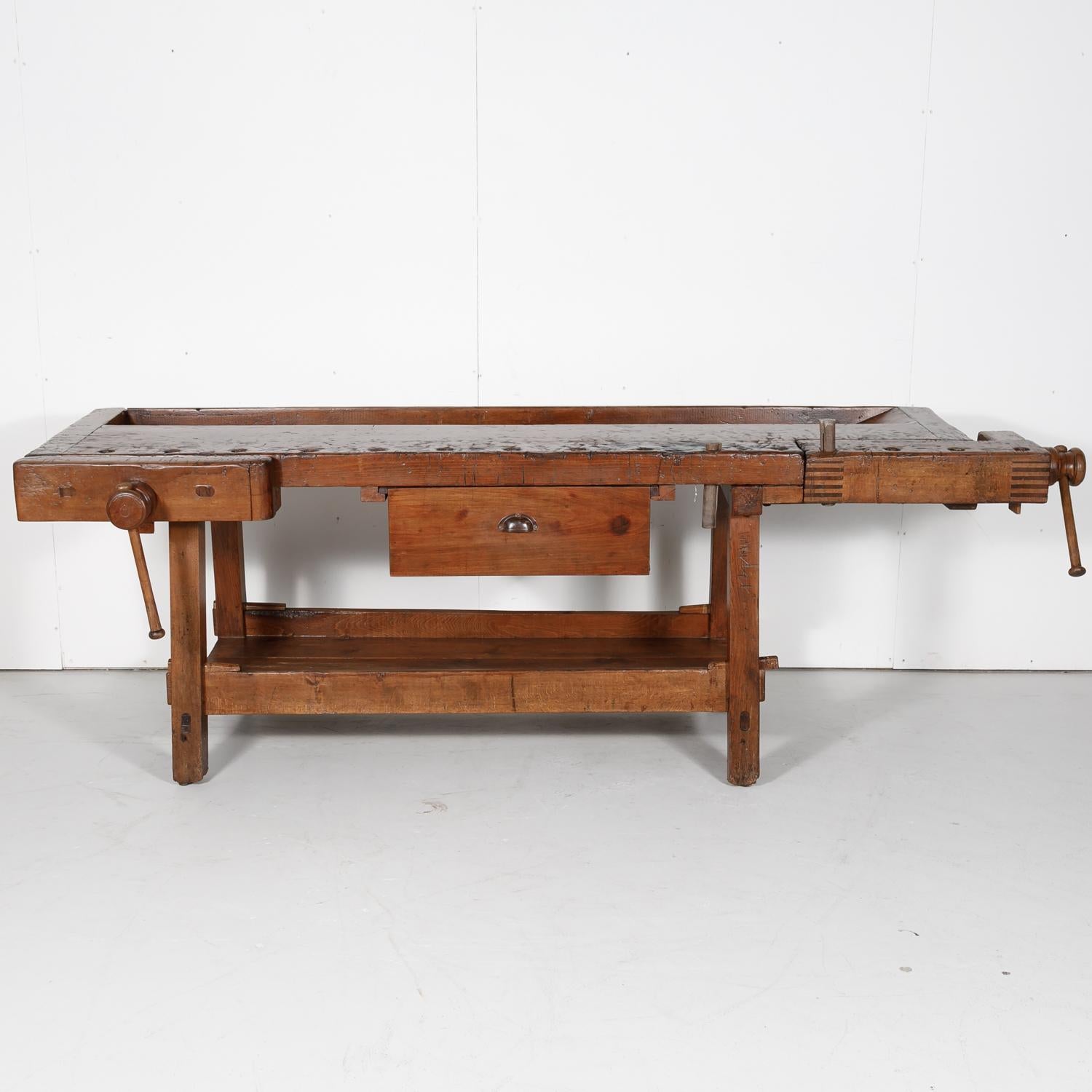 19th century French etabli or carpenter's workbench hand constructed of pine and chestnut in the South of France near Uzés, having a top that is almost five inches thick, trestle legs, and a bottom shelf. The surface of this rustic carpenter's