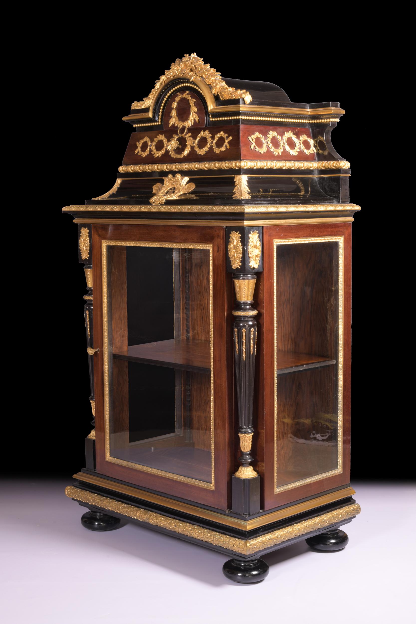 An exceptional 19th century ormolu mounted ebonised and amaranth vitrine.

The domed cresting surmounted by a festoon of oak leaves above a frieze of garlands including a drawer with a ribbon-tied cartouche, the glazed lower part with turned