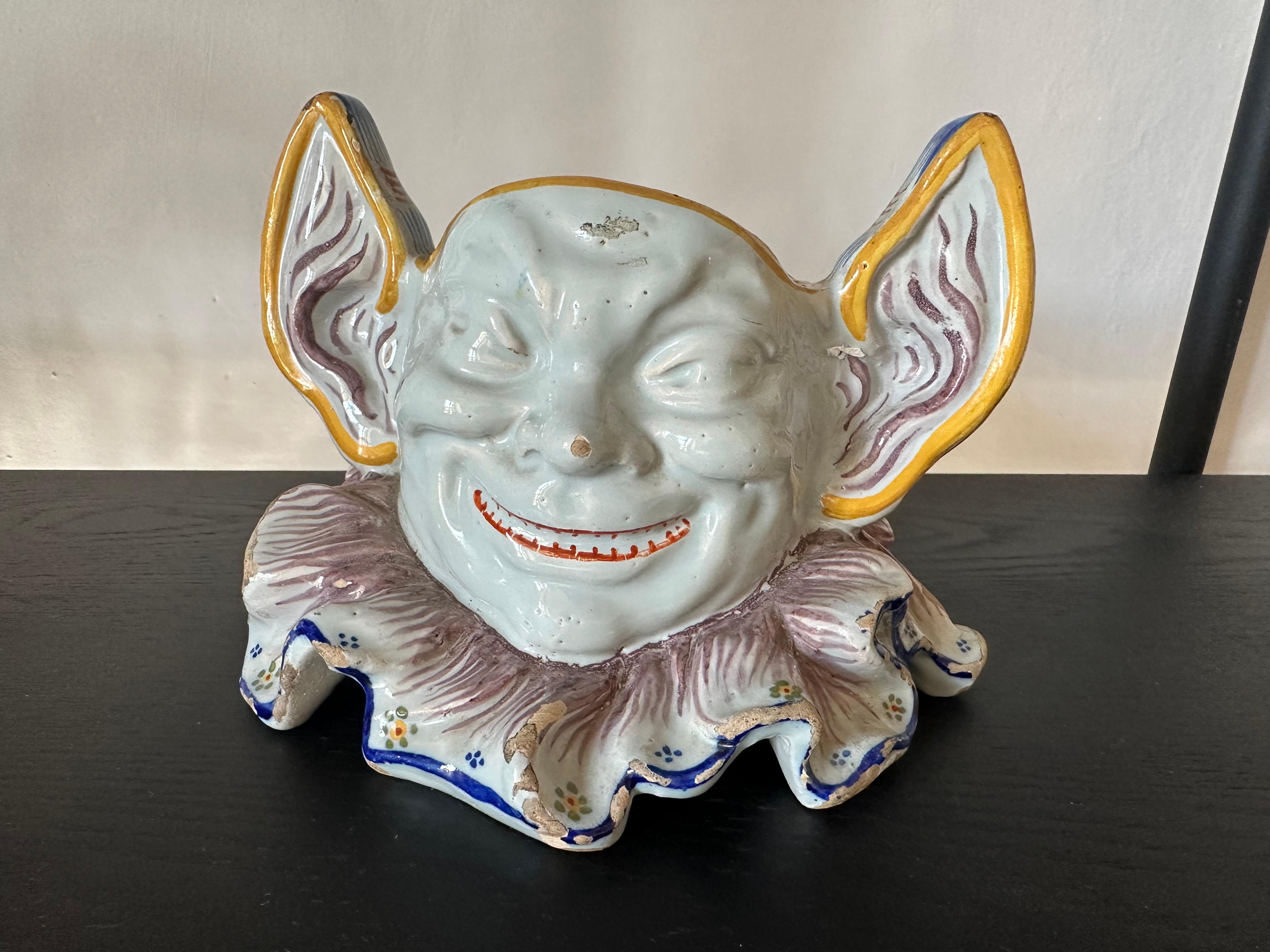 Cet exceptionnel cache-pot en faïence française du XIXe siècle provenant de Rouen est une pièce rare et fantaisiste qui témoigne de l'art et de l'humour de son époque. Conçu comme un personnage arlequin ou diabolique, le cache-pot présente un visage
