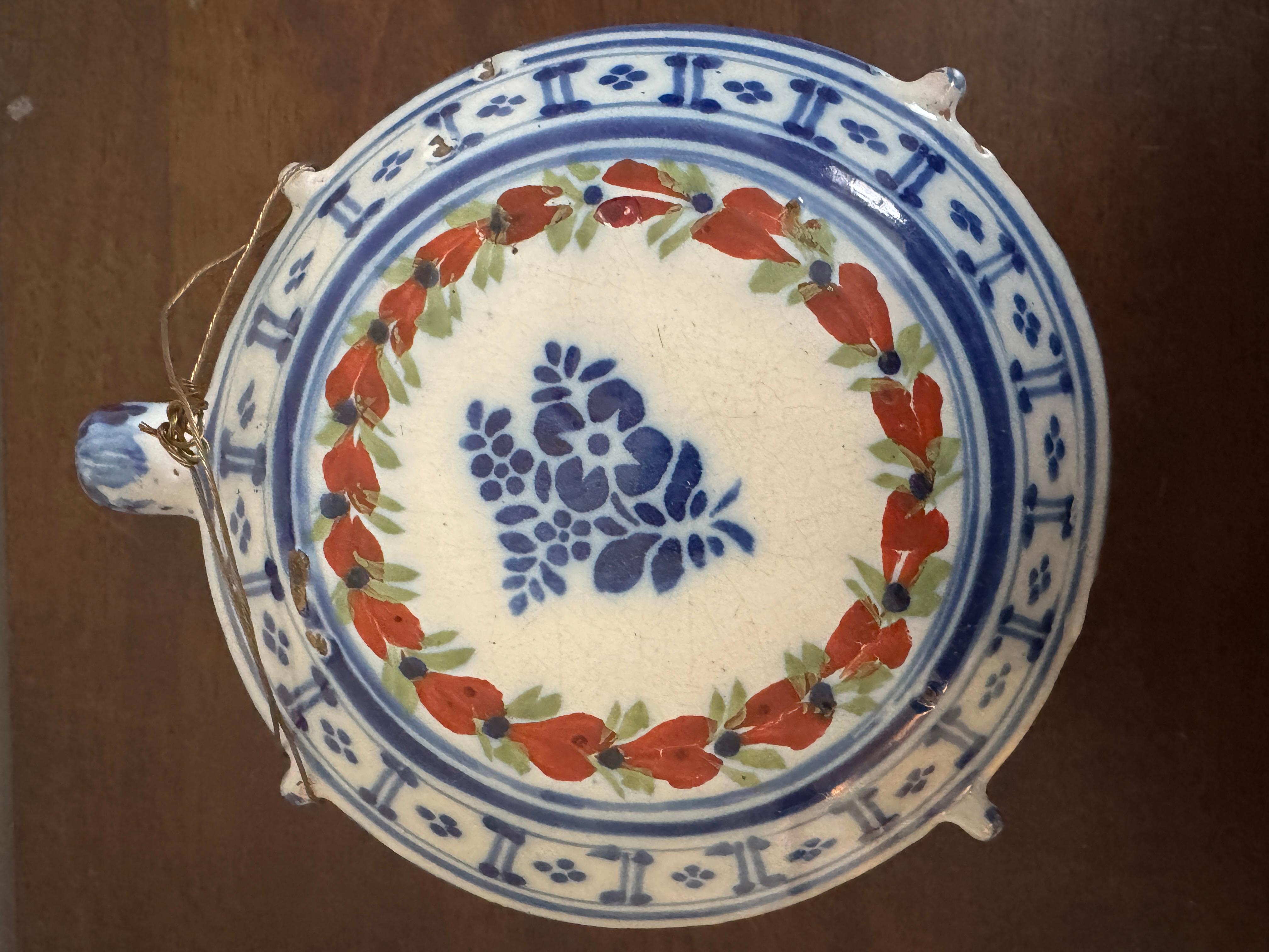 Frasco de peregrino de loza francesa del siglo XIX, de forma tradicional pintado con rocíos de flores rojas y verdes dentro de bordes azules.