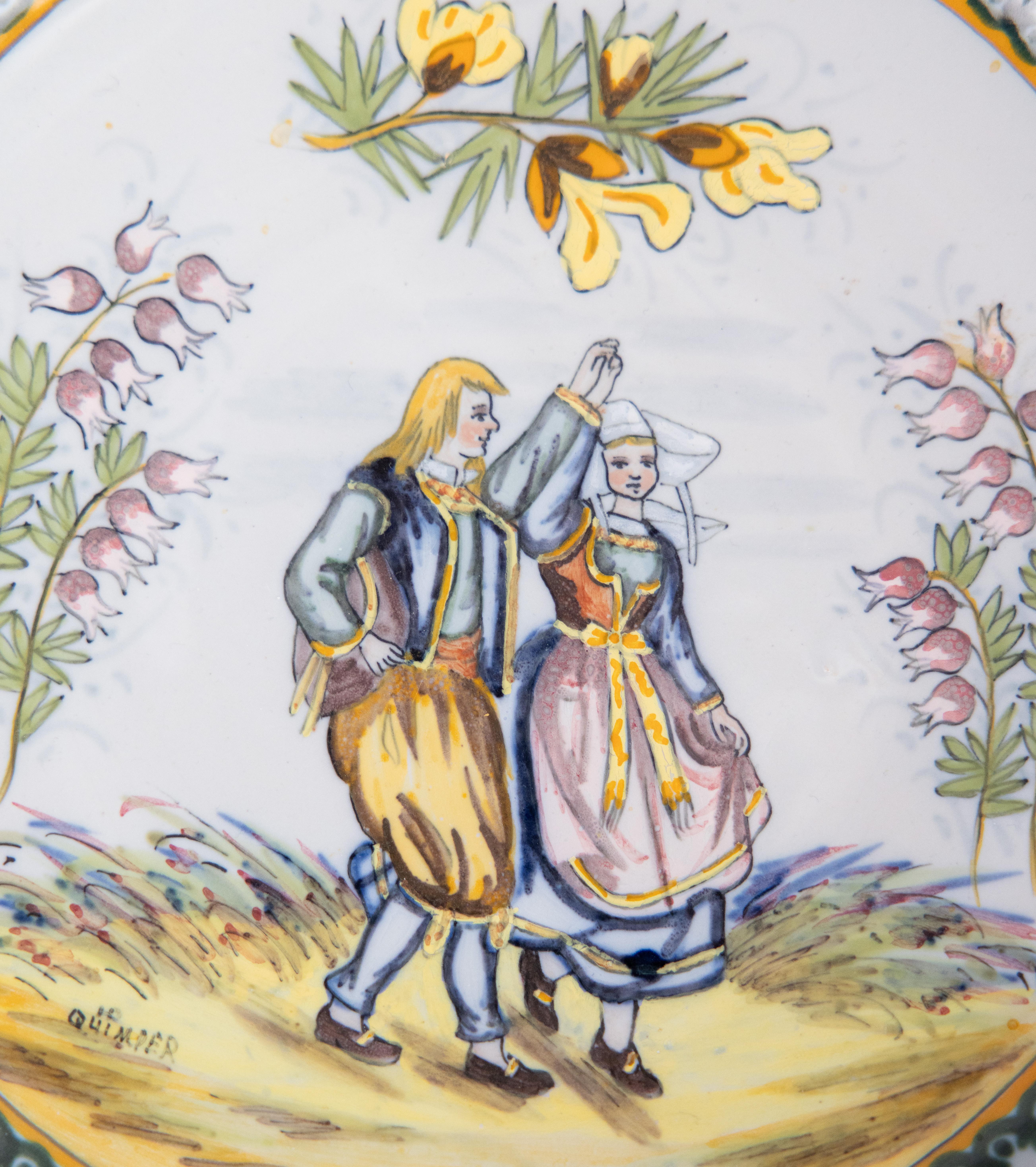 A charming antique French faience Quimper pie crust plate, circa 1895. Maker's mark on front and reverse. This lovely plate features a finely detailed hand painted Breton couple in traditional costume dancing. The sweet couple is surrounded by pink