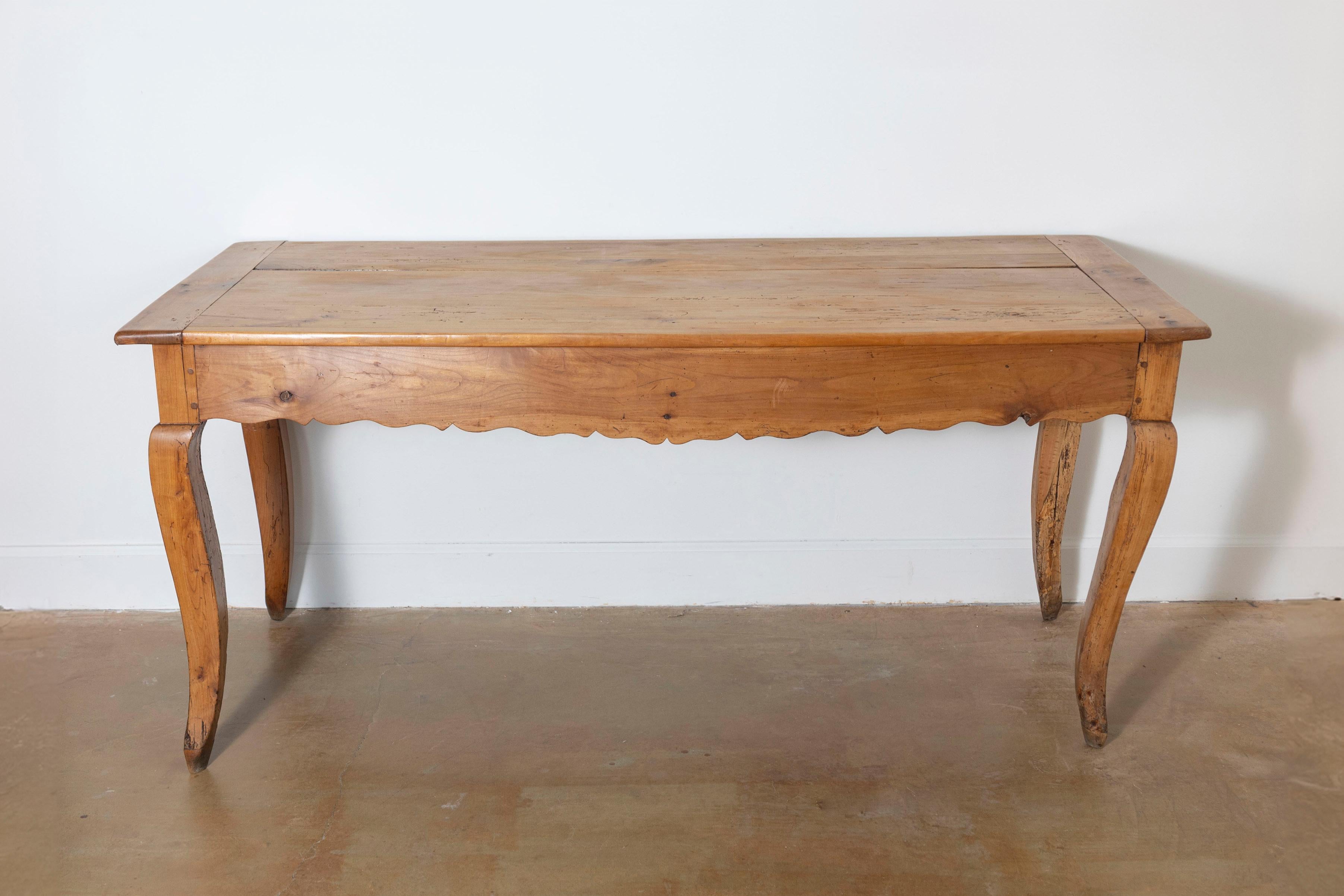 Cette table de ferme française du XIXe siècle est un charmant exemple d'artisanat rustique et de fonctionnalité. Construite en bois de cerisier, la table présente une patine chaude et vieillie qui met en valeur le grain naturel et le caractère du