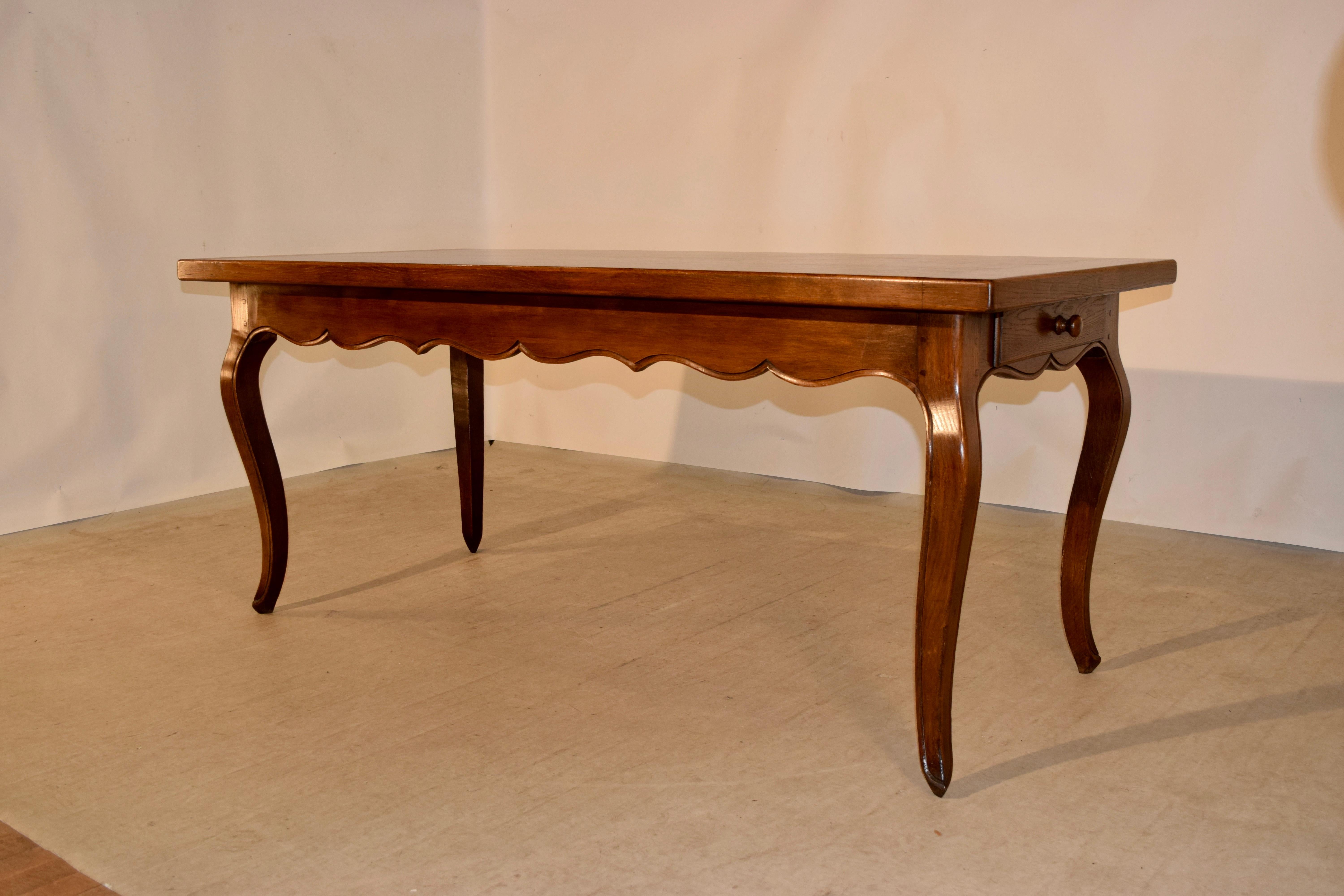 19th century farm table from France. The top is very thick and measures 1.75 inches in thickness, and is banded and follows down to a scalloped apron with a molded edge and two drawers, one on each end, supported on hand-turned cabriole legs with