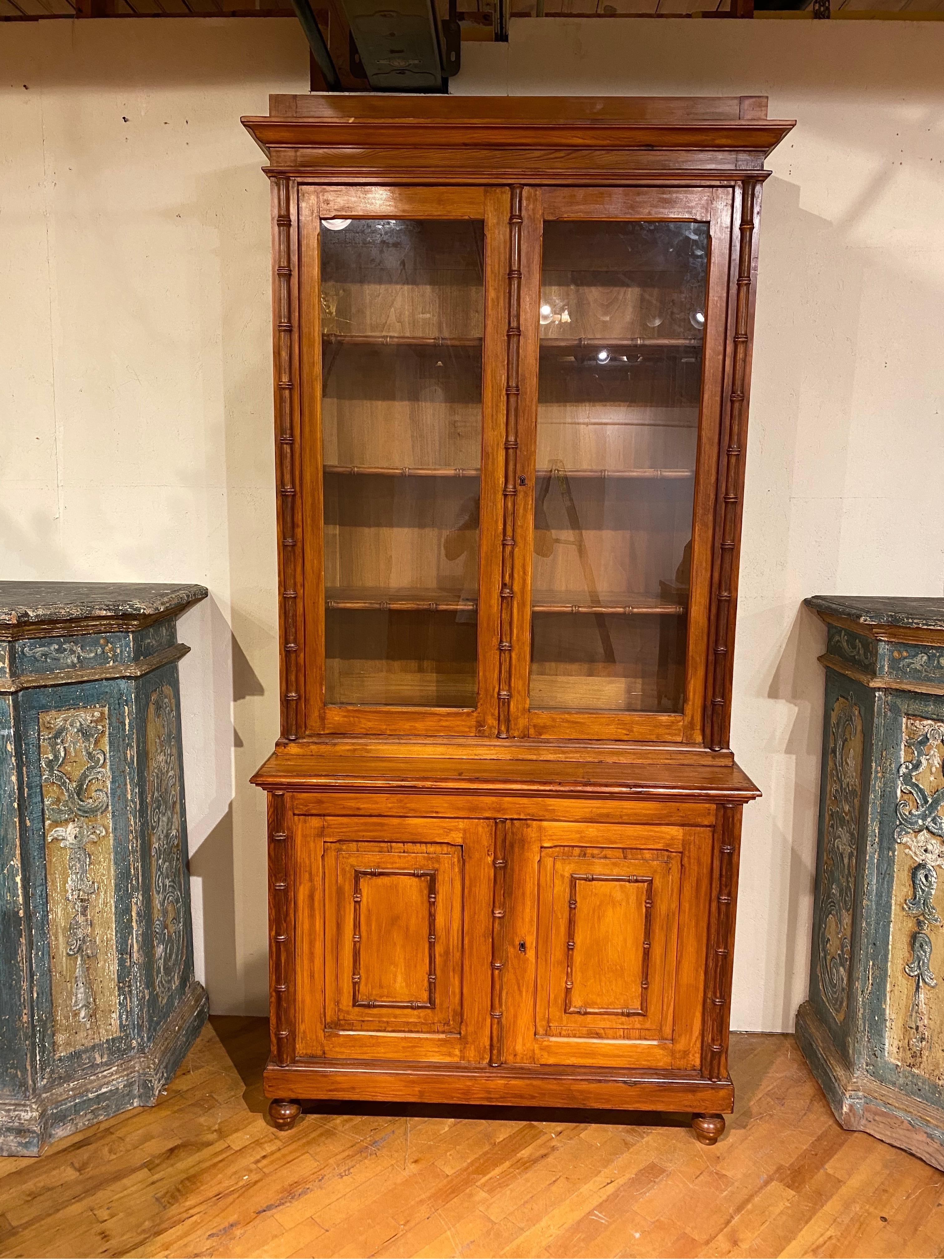 19th century French faux bamboo and pine cabinet. Great quality 2 piece cabinet resting on ball feet with blind paneled doors framed in faux bamboo on the bottom and glass front on top. Shelves have bamboo molding as well.