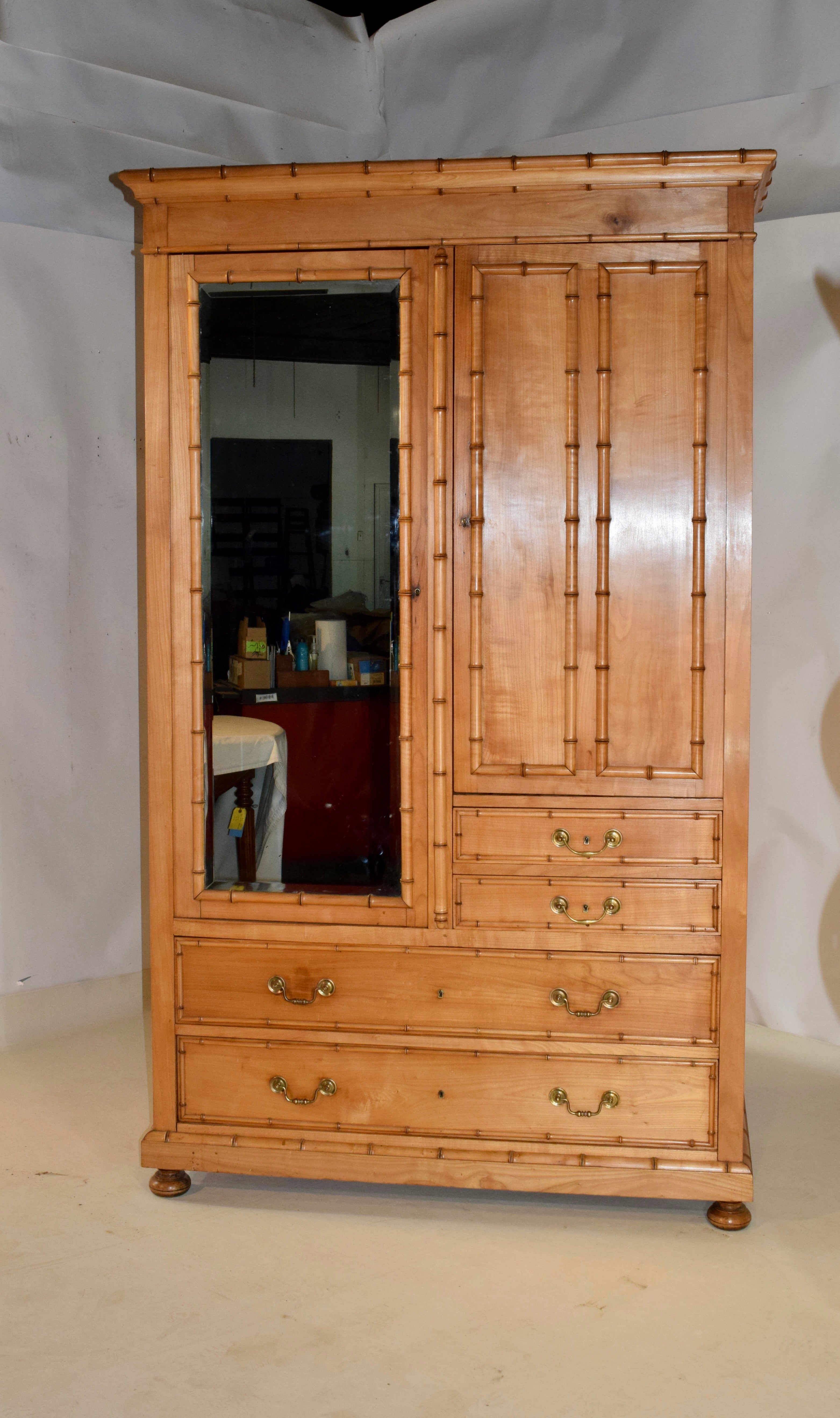 19th century French cherry armoire with faux bamboo details. the crown has faux bamboo moldings over a single mirrored door on the left, which opens to reveal a bar for hanging clothing and a single door on the right, which opens to reveal shelving.