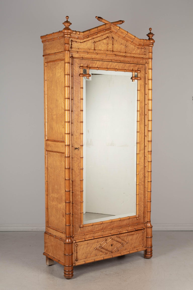 A 19th century French faux bamboo armoire, or wardrobe, made of birdseye maple with solid cherry faux bamboo details and mirrored door. Turned wood finials and realistic looking bamboo design. Beveled mirror door opens to an interior with five