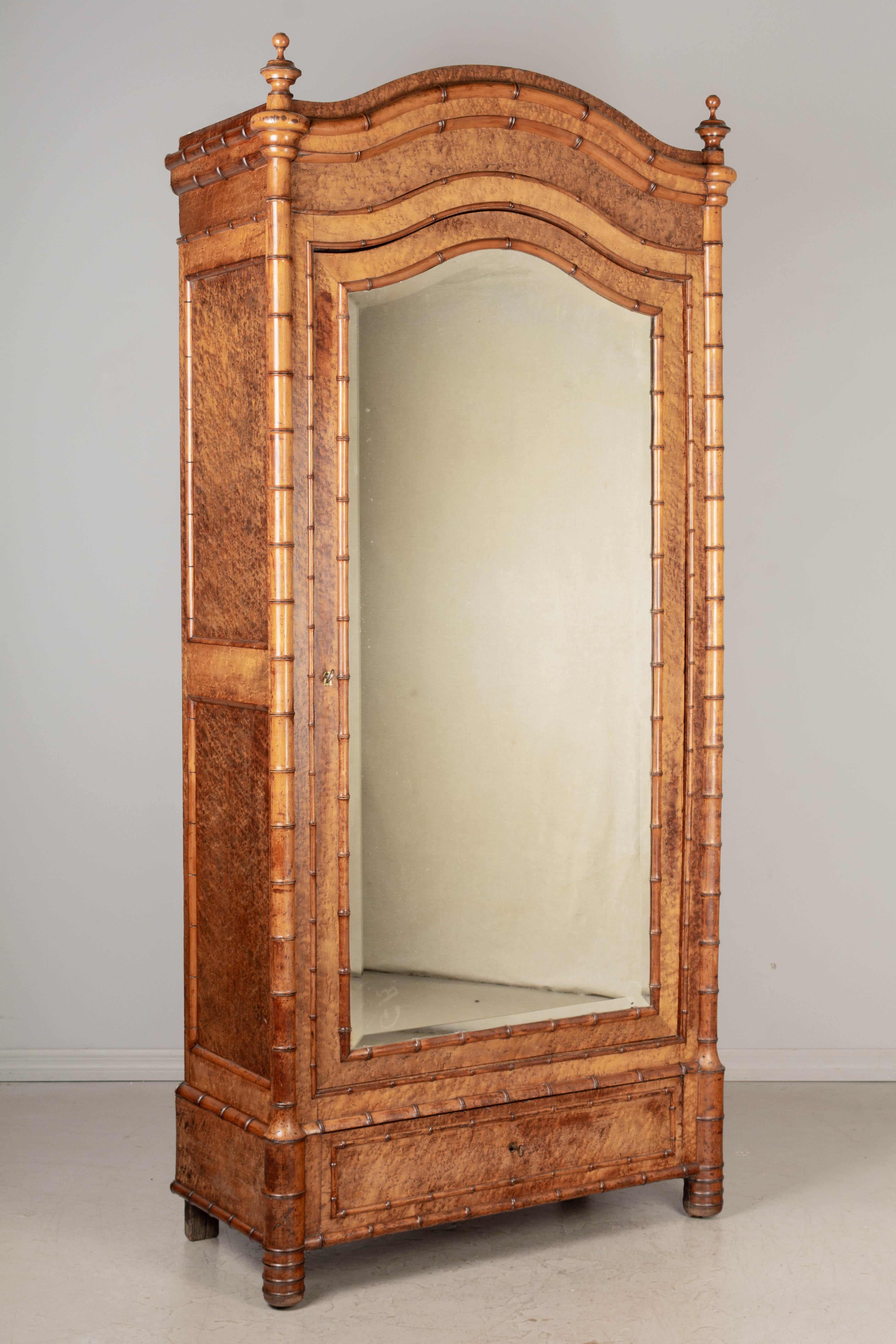 A 19th century French Napoleon III faux bamboo armoire, or wardrobe, made of birdseye maple with solid cherry faux bamboo details, chapeau de gendarme crown and beveled mirror door. Large turned wood finials and realistic looking bamboo design.