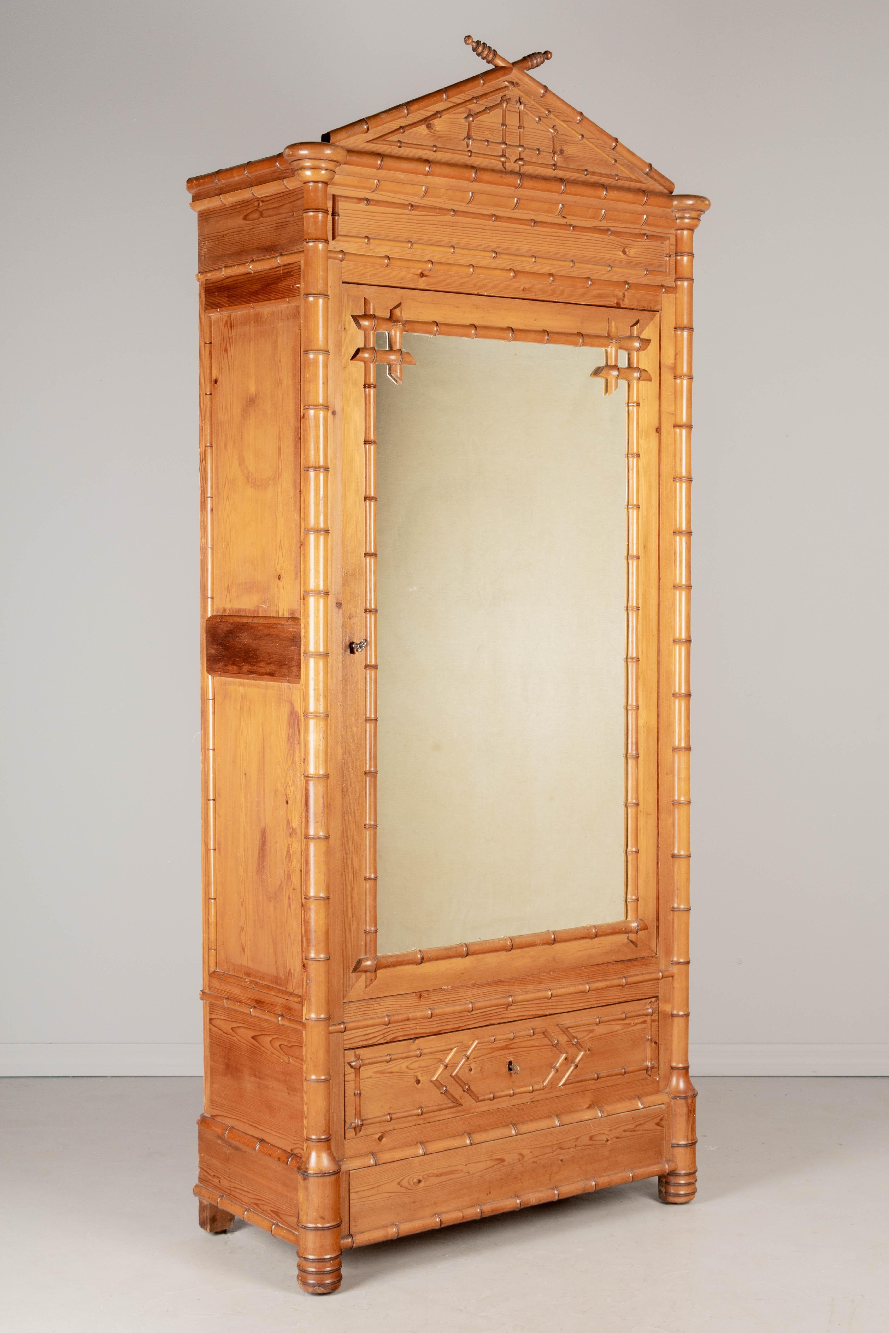 A 19th century French faux bamboo armoire, or wardrobe, made of pine with solid cherry faux bamboo details and oak back. Mirrored door opens to an interior with three adjustable shelves. Two dovetailed drawers below the door. Working locks and two