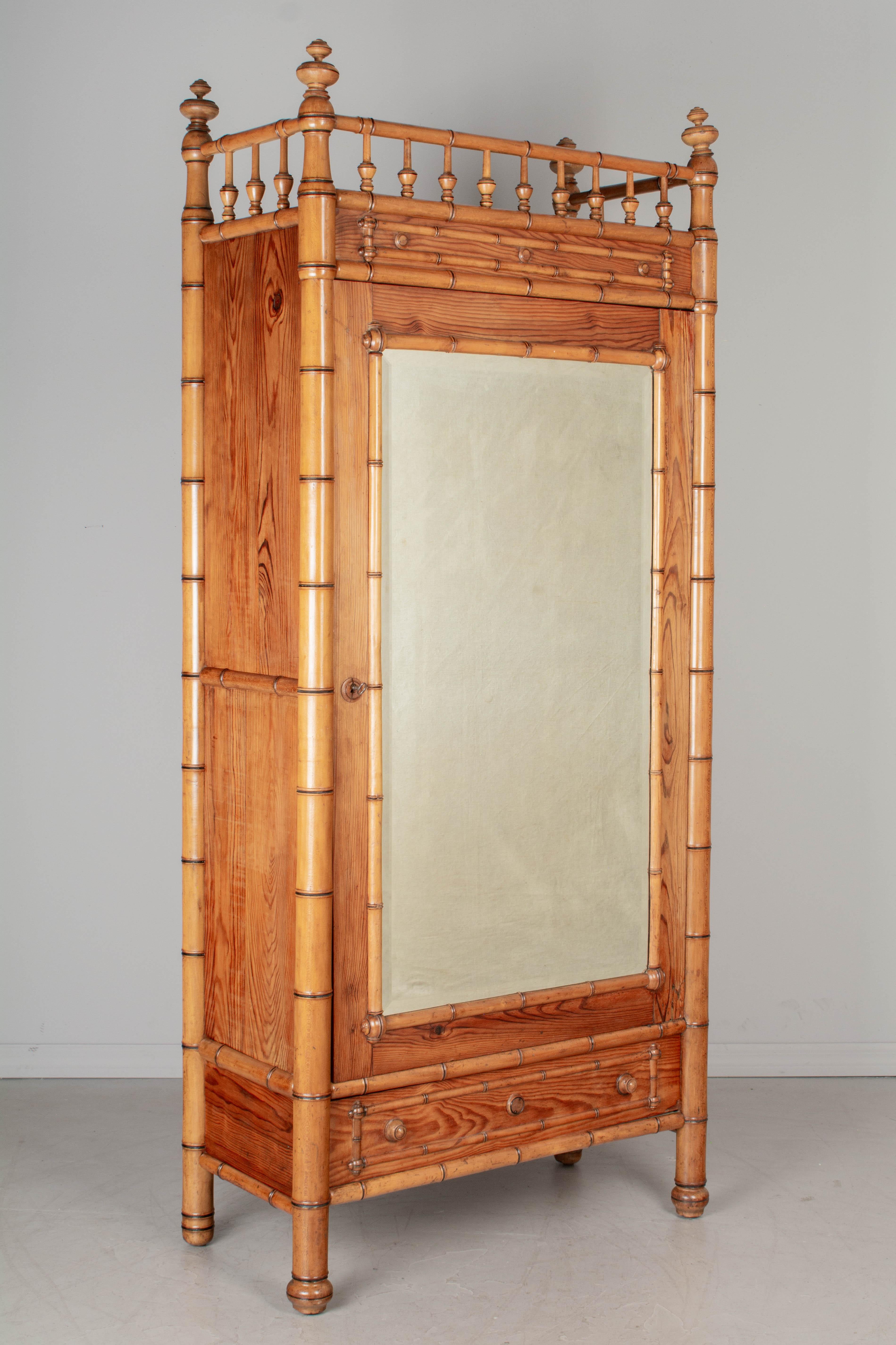 A 19th century French faux bamboo armoire, or wardrobe, made of pitch pine with solid beechwood faux bamboo details. Beveled mirror door opens to an interior with three adjustable shelves. One dovetailed drawer below the door. Working lock and key.