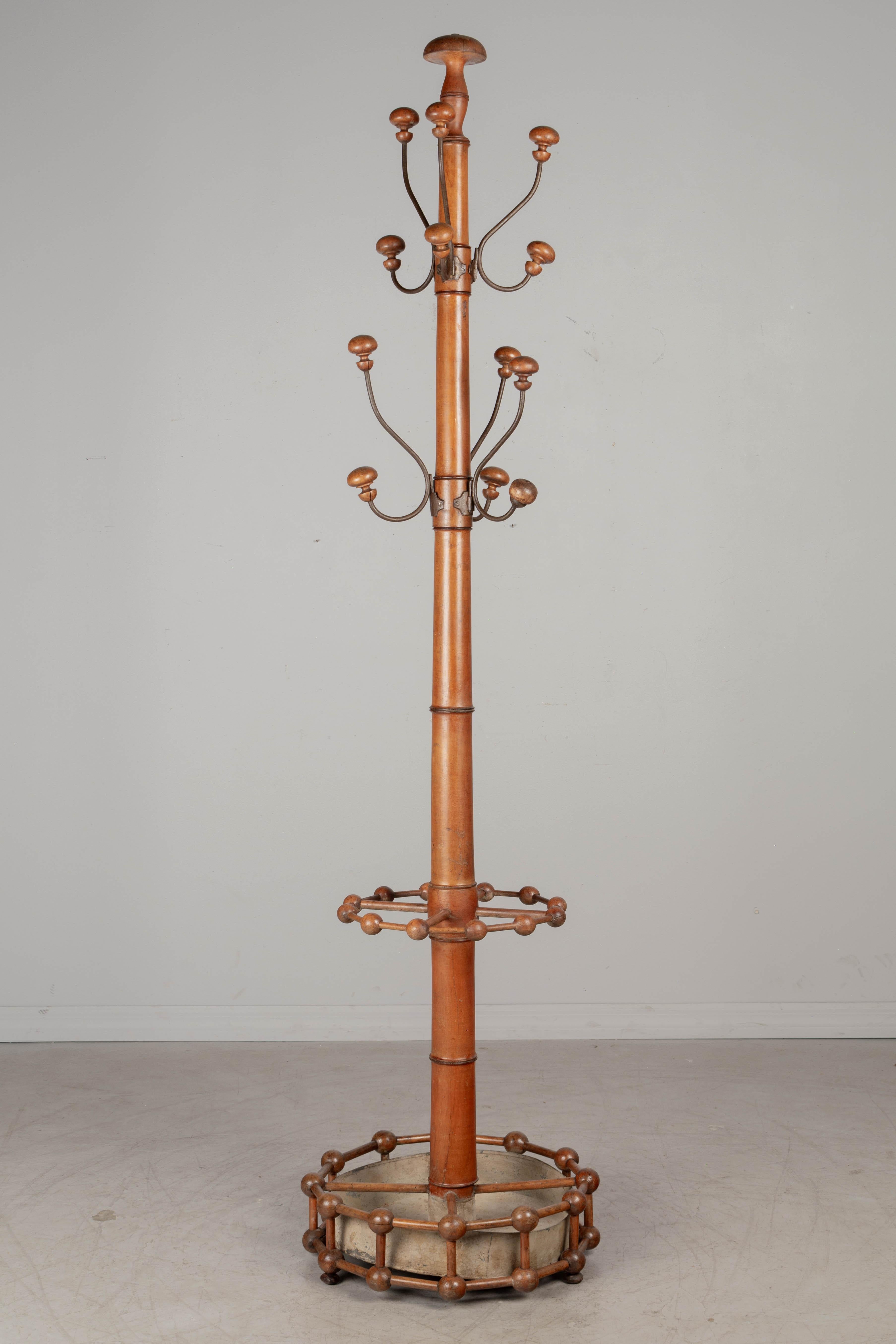 A 19th century French faux bamboo hall tree, or coat rack, made of beech wood. Large, sturdy tapered turned center pole with six metal hooks, each with two large turned pegs for hanging hats and coats. One hook repaired. Circular base with ball and