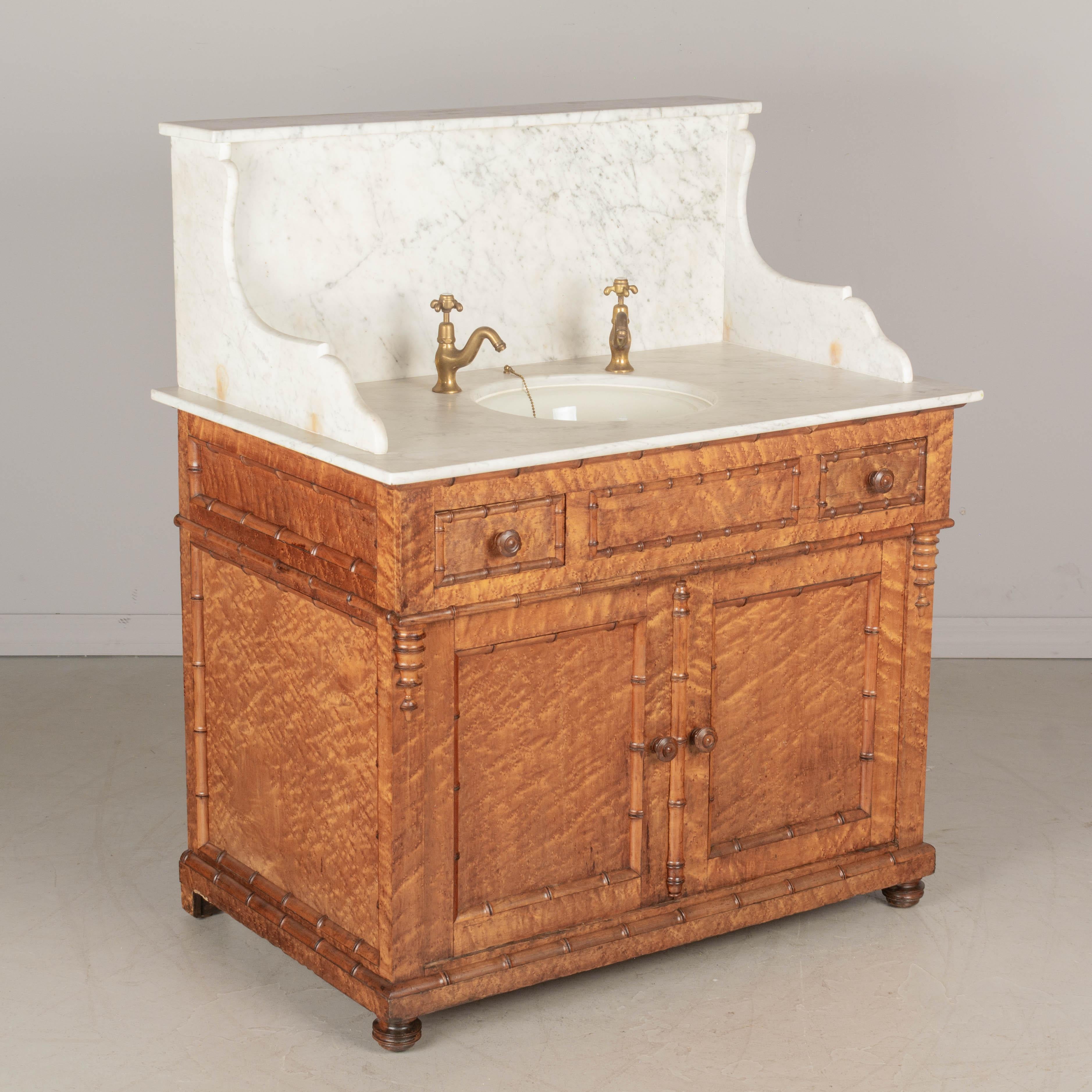 A 19th century French faux bamboo marble top bathroom vanity. Made of solid oak with birdseye maple veneer and carved turned cherry wood faux bamboo decorative trim. Two dovetailed drawers and a cabinet below, opening to one new interior shelf and